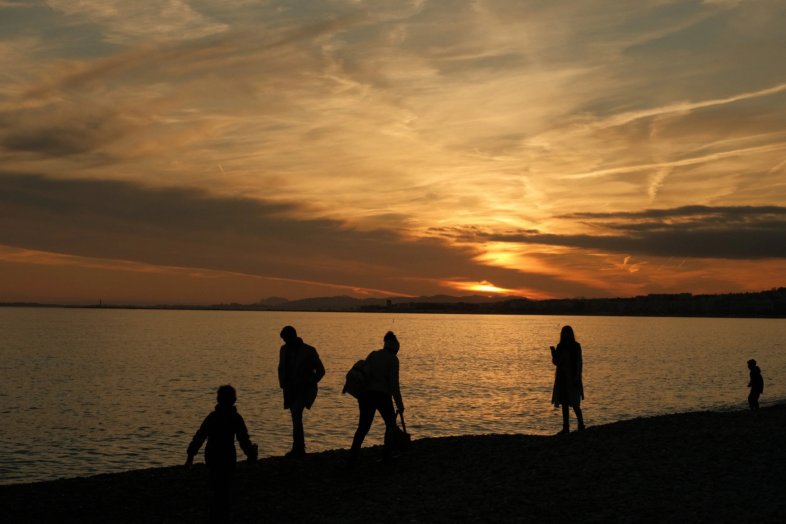 Silhouettes de personnes au bord de l'eau lors d'un coucher de soleil avec un ciel orageux.