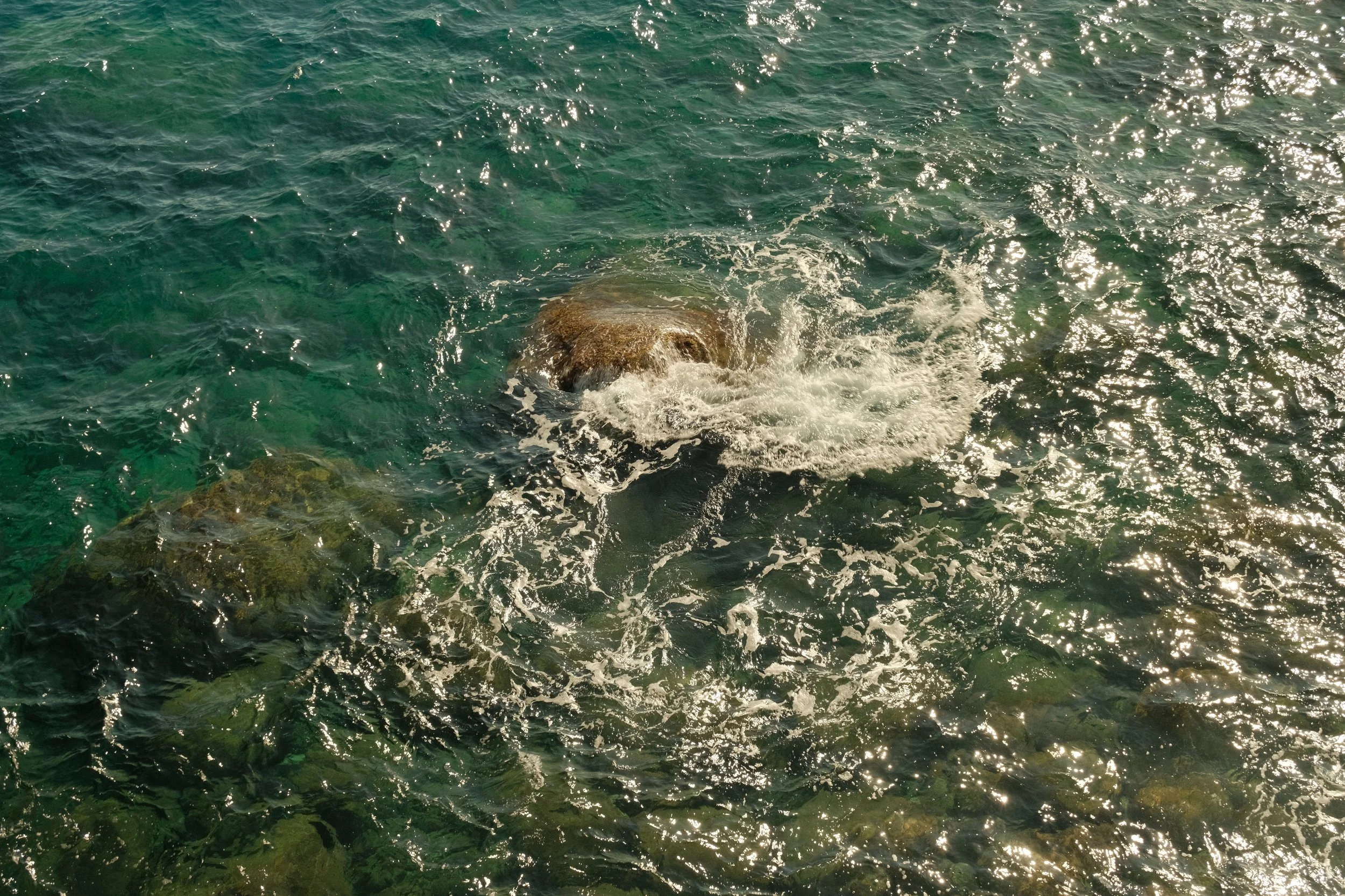 L'eau de la mer claire avec des rochers visibles sous la surface, reflétant la lumière du soleil.