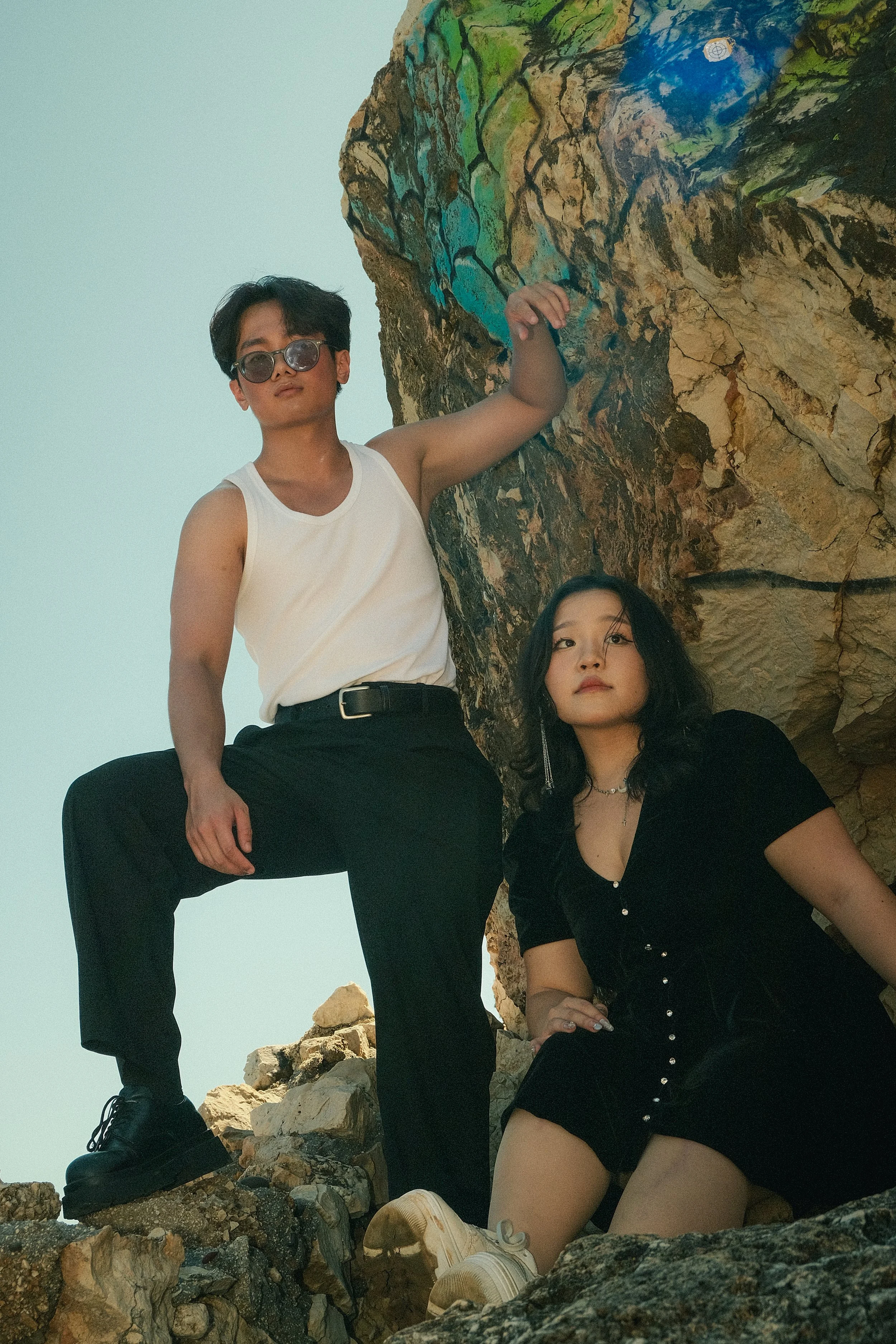 Deux jeunes femmes posent devant une roche colorée en extérieur, l'une debout avec une main sur la roche, l'autre assise sur des rochers.