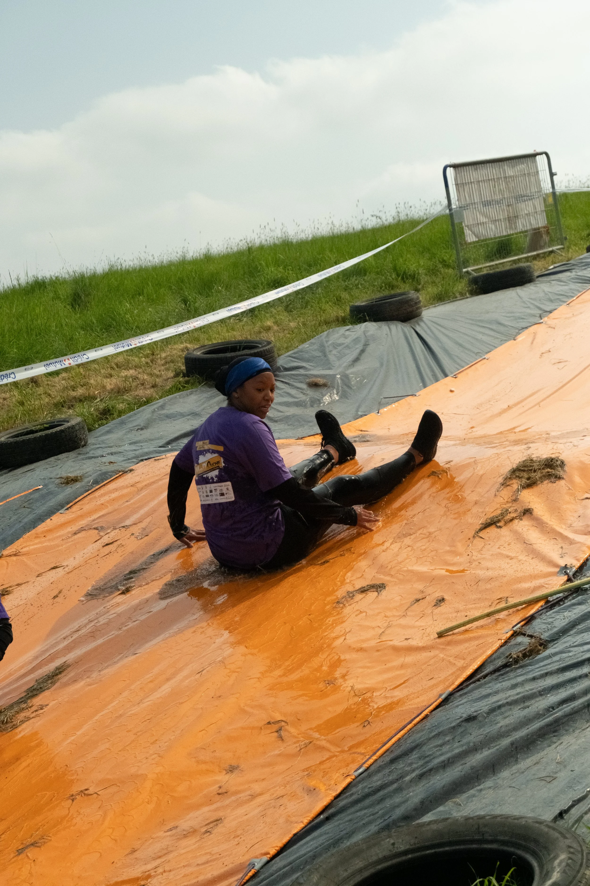 Une femme portant un t-shirt violet glisse sur une luge orange lors d'une activité extérieure, avec du gazon vert en arrière-plan.