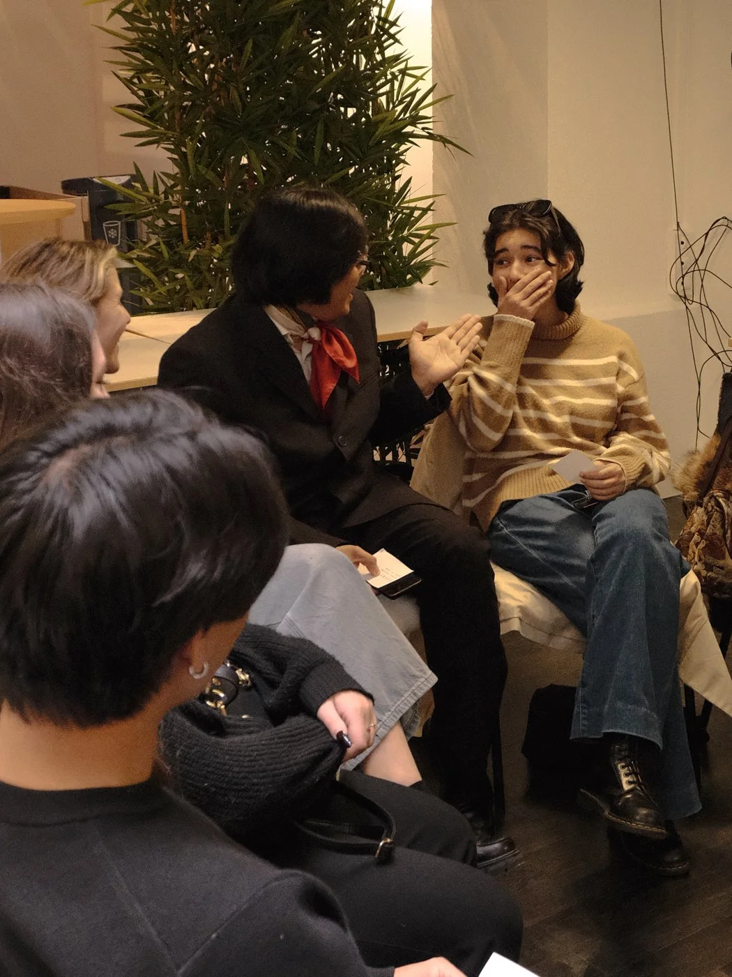 Groupe de jeunes discutant ensemble dans un endroit intérieur, avec un arbre décoratif en arrière-plan.