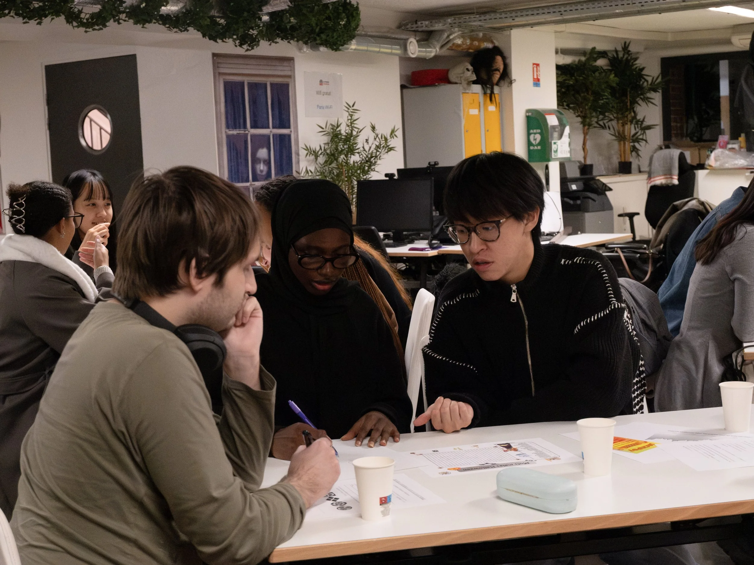 Groupe de personnes discutant autour d'une table en intérieur, avec ordinateurs et papiers