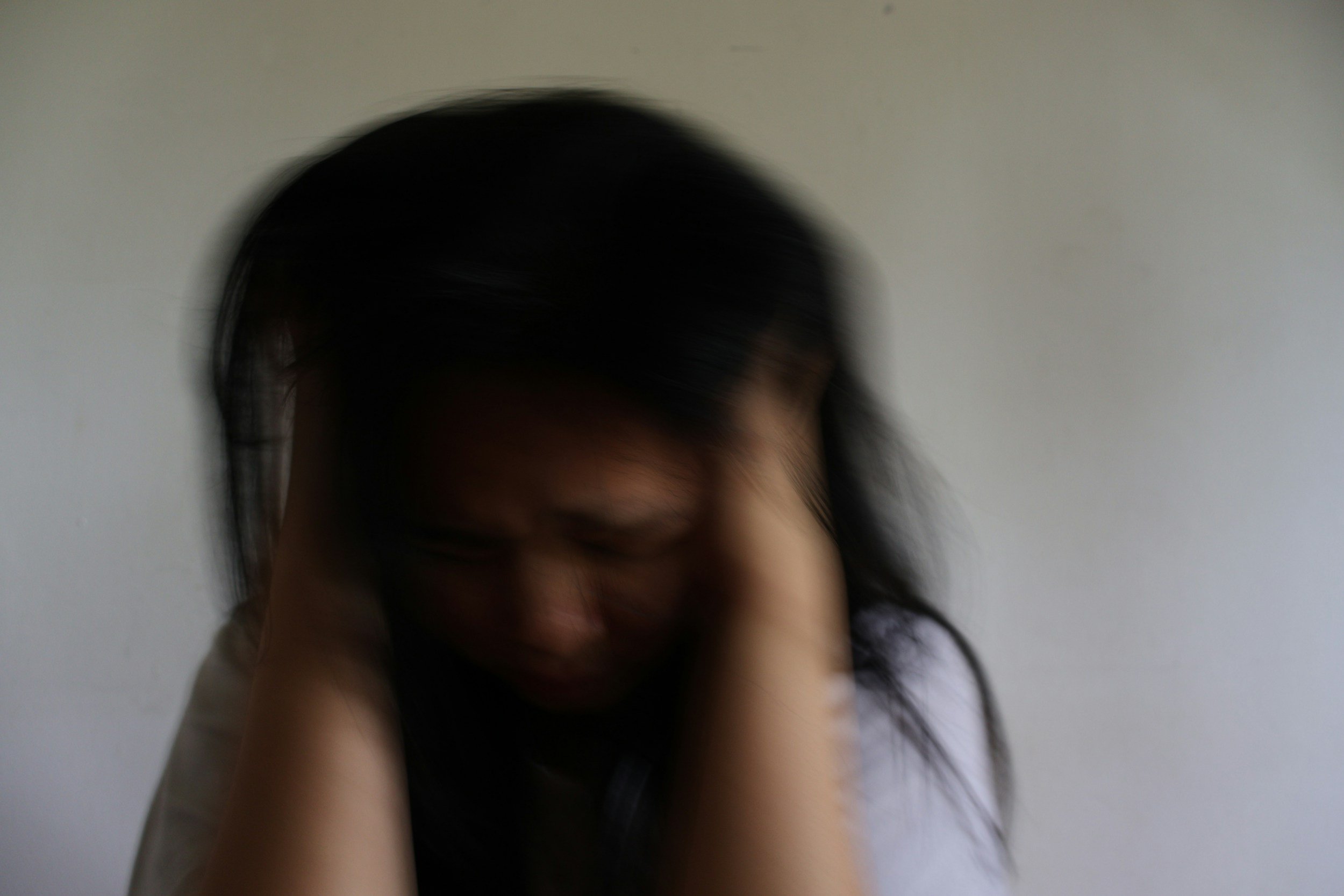 A person with dark hair holding their head, appearing distressed or overwhelmed, against a plain background.