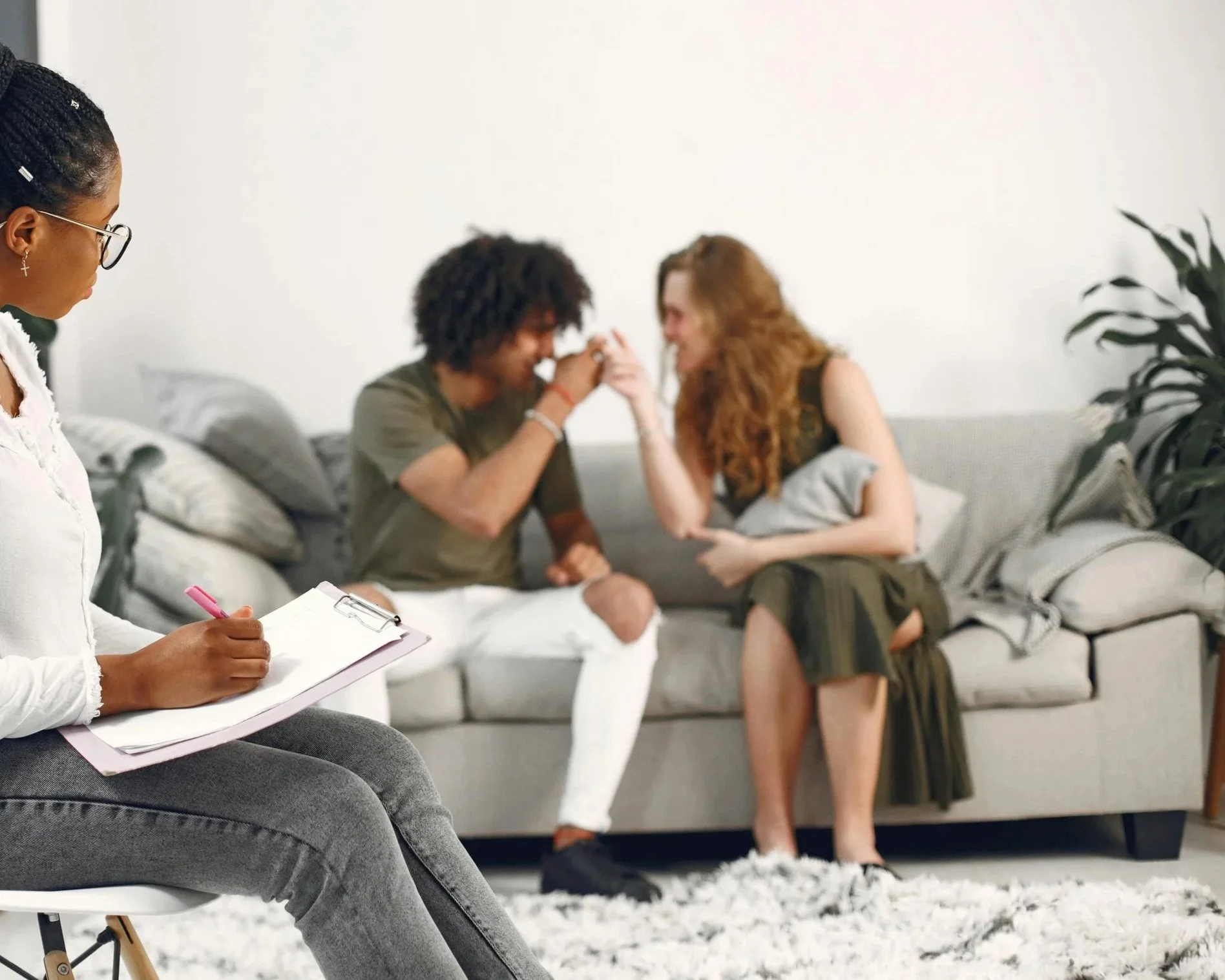 A therapist taking notes while a couple shares intimate moment during therapy session in a living room.