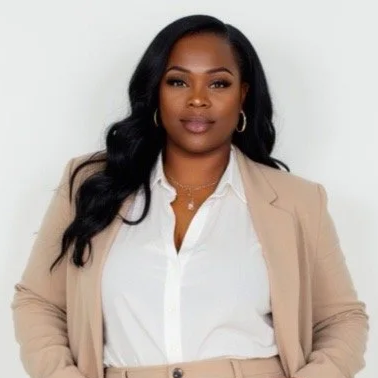 A woman with glasses and hoop earrings smiling indoors.