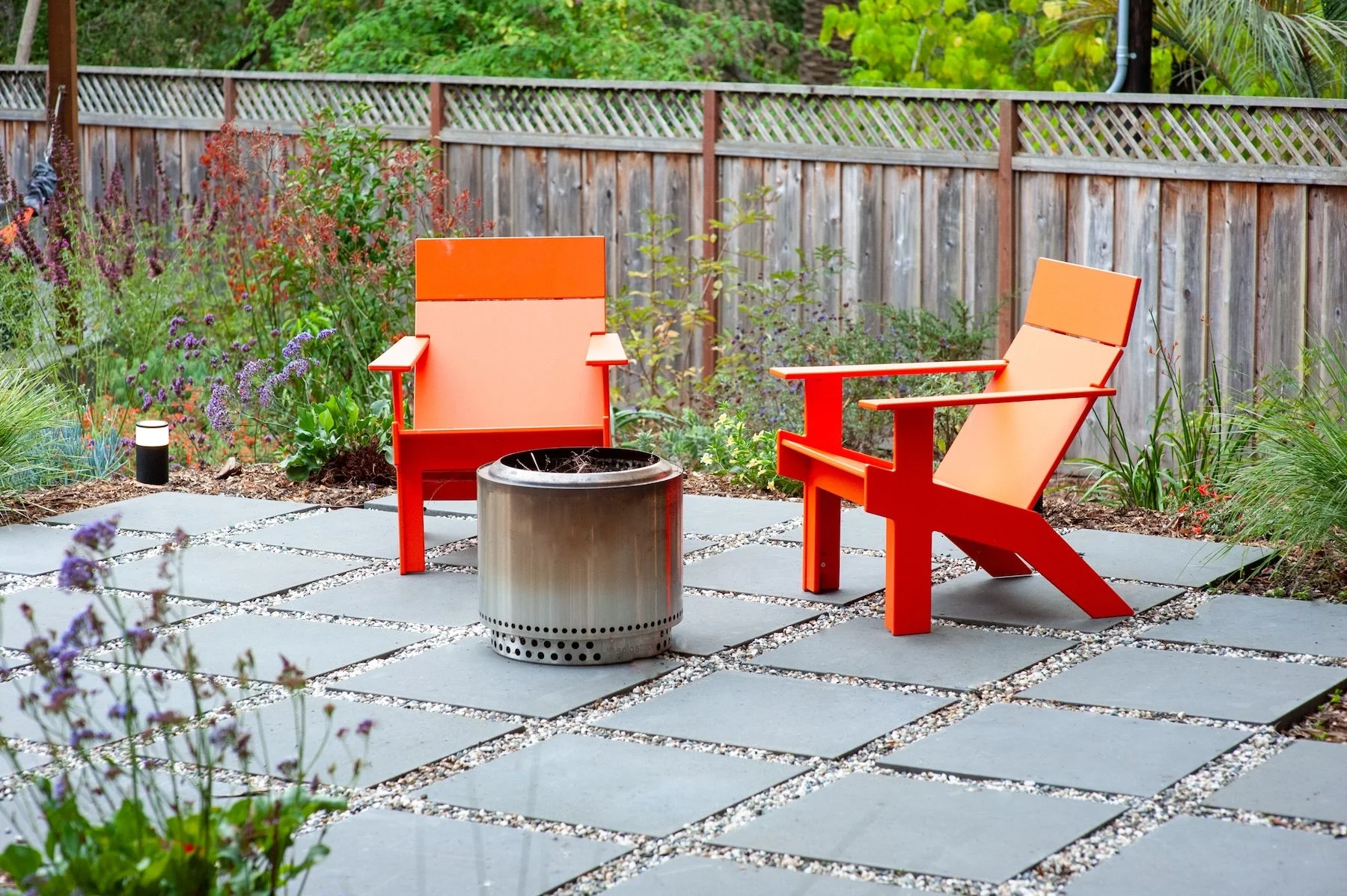 Orange modern Adirondack chairs around a steel fire pit on a bluestone and gravel patio - Orchard Keepers