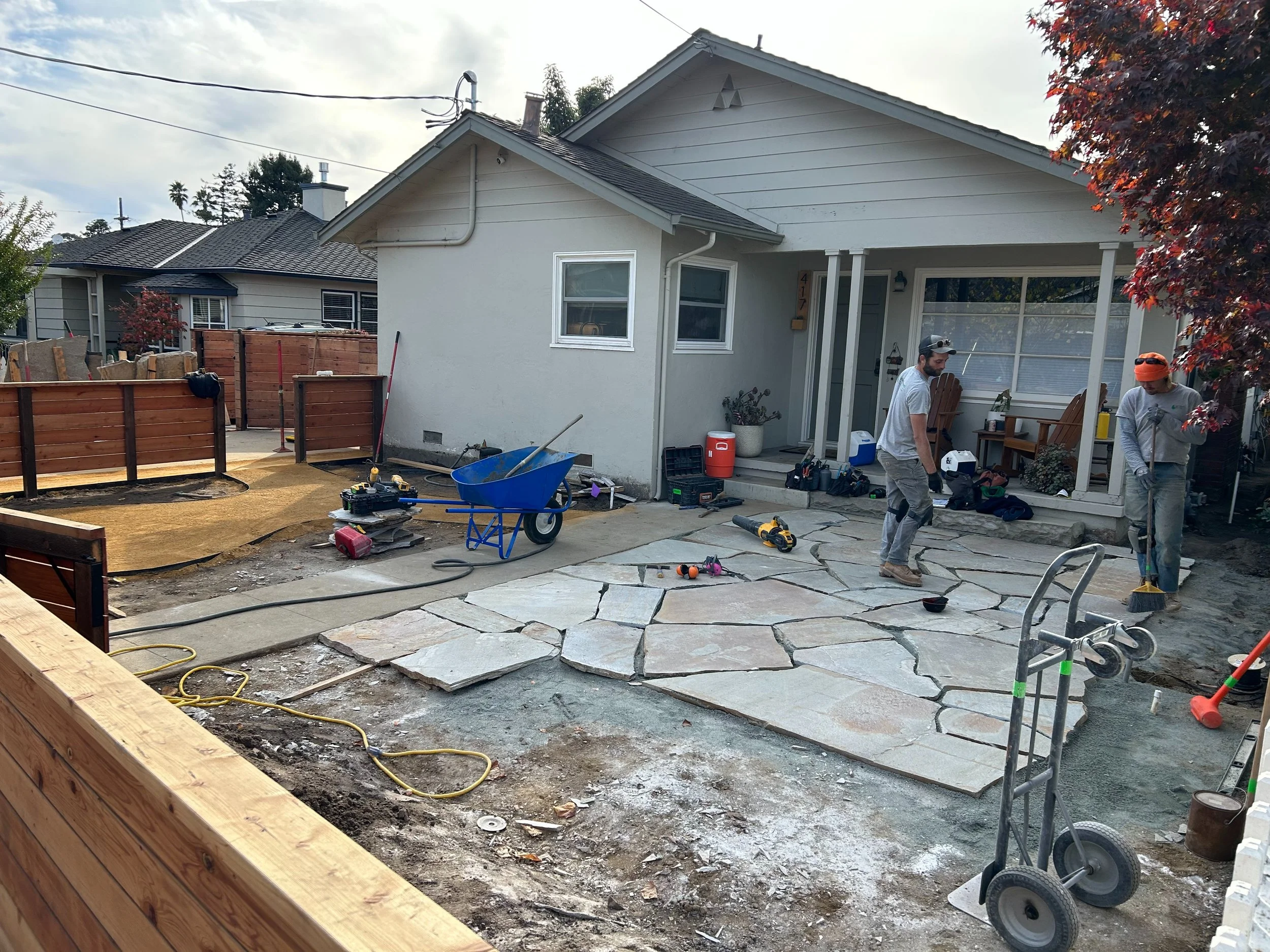 Workers installing a flagstone patio in a front yard landscape renovation with wheelbarrows and tools