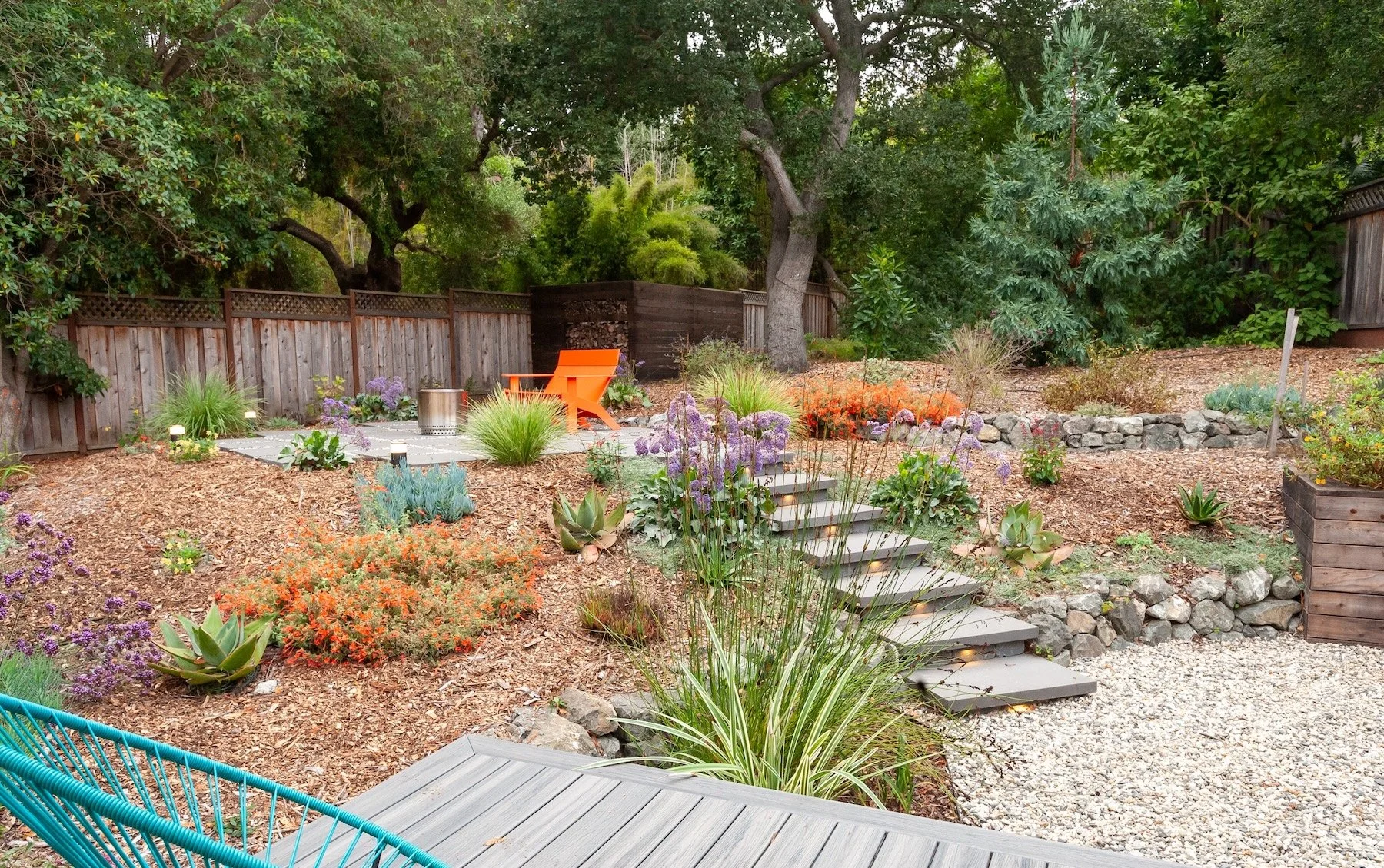 Terraced backyard landscape with drought-tolerant plants, stone steps, and gravel path leading to a wood deck - Orchard Keepers