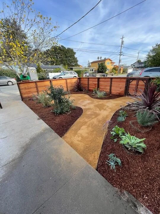 Completed side yard landscape with a paver walkway and fresh planting beds along a wood fence - Orchard Keepers