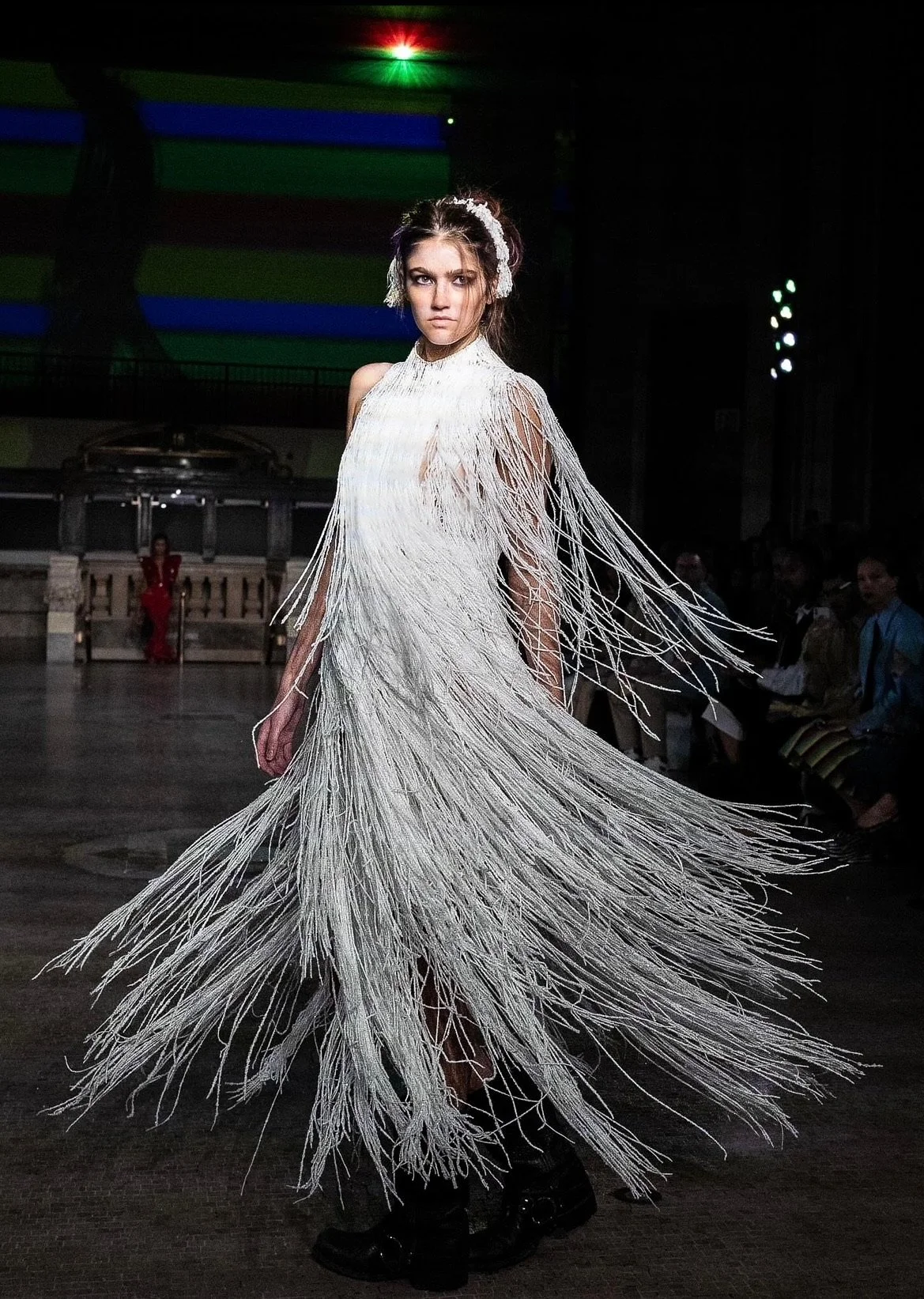Fashion model walking on runway wearing a white dress made of strings or threads with fringe details.