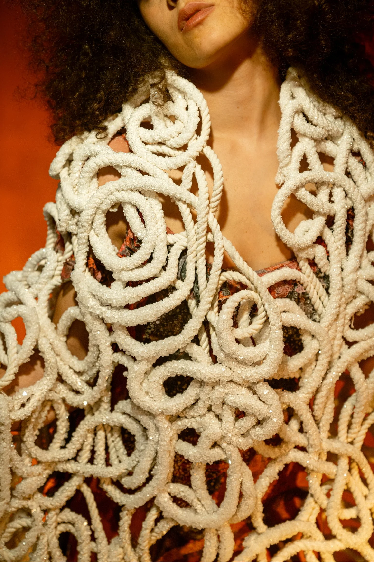 A woman with curly hair wearing a garment made of intertwined, salt-covered ropes.