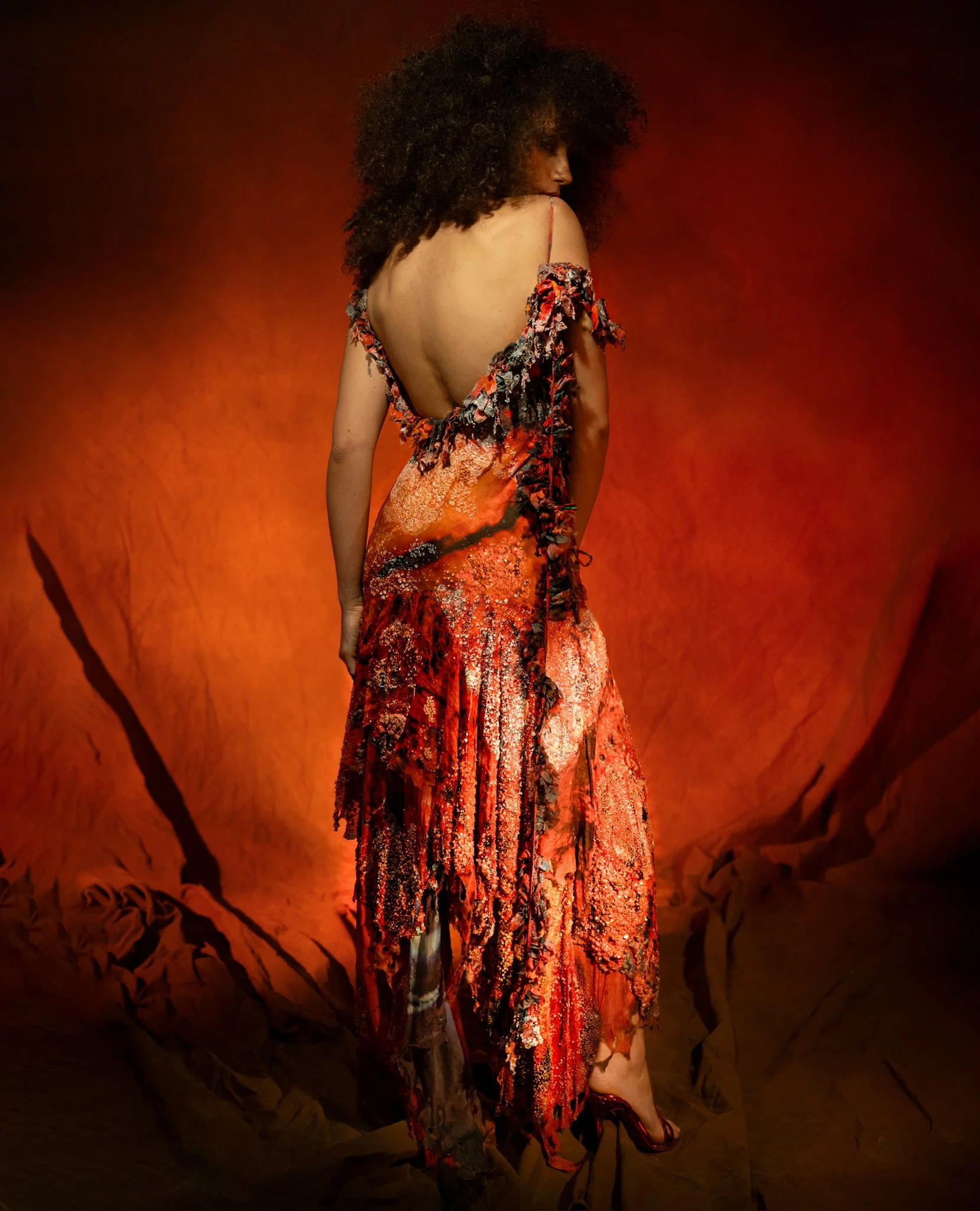 A woman in an elaborate red and black dress with a deep back stand against an orange backdrop.
