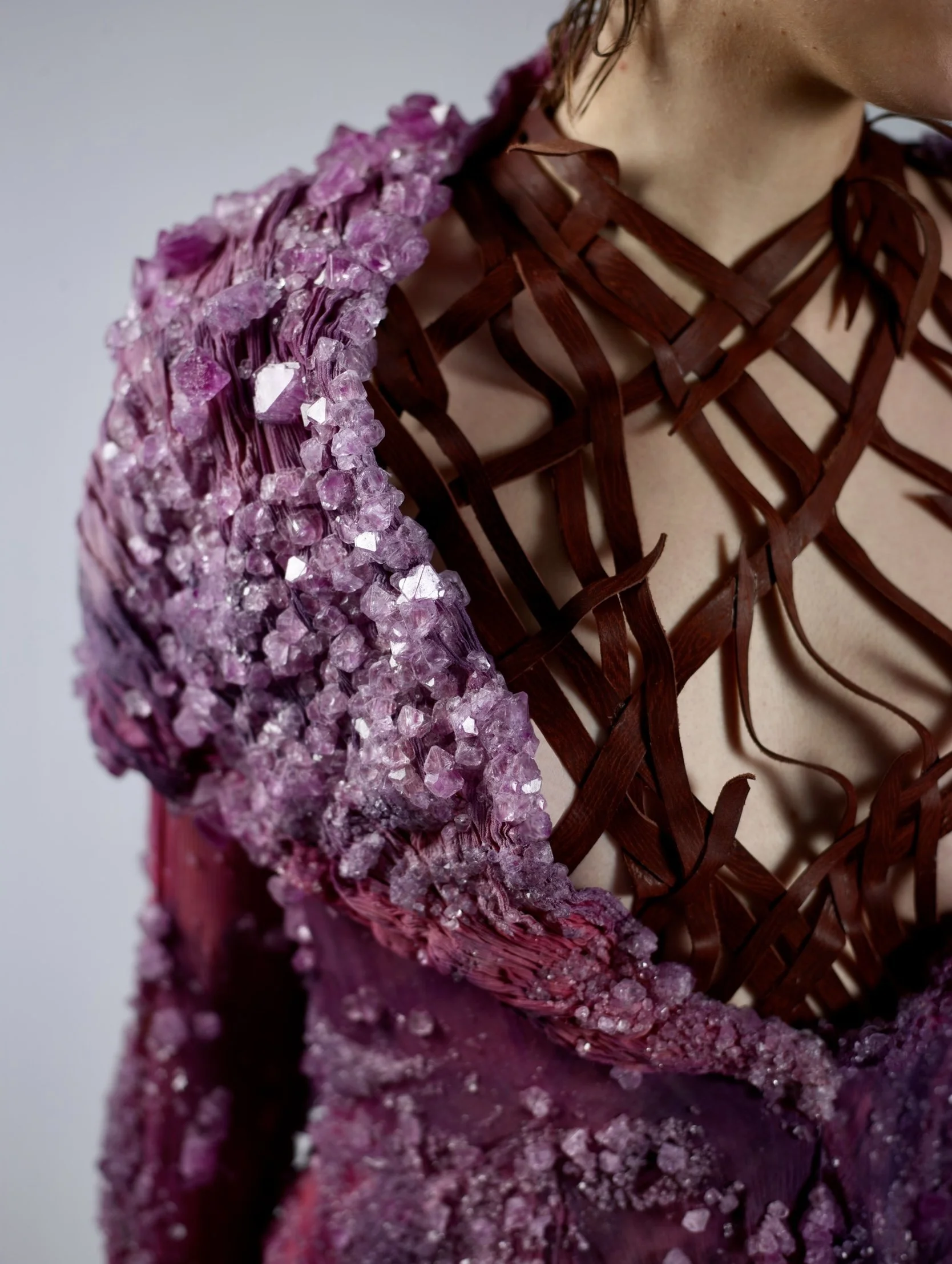 Close-up of a fashion garment featuring a purple crystal-encrusted sleeve and a red wooden lattice design across the chest and shoulder area.