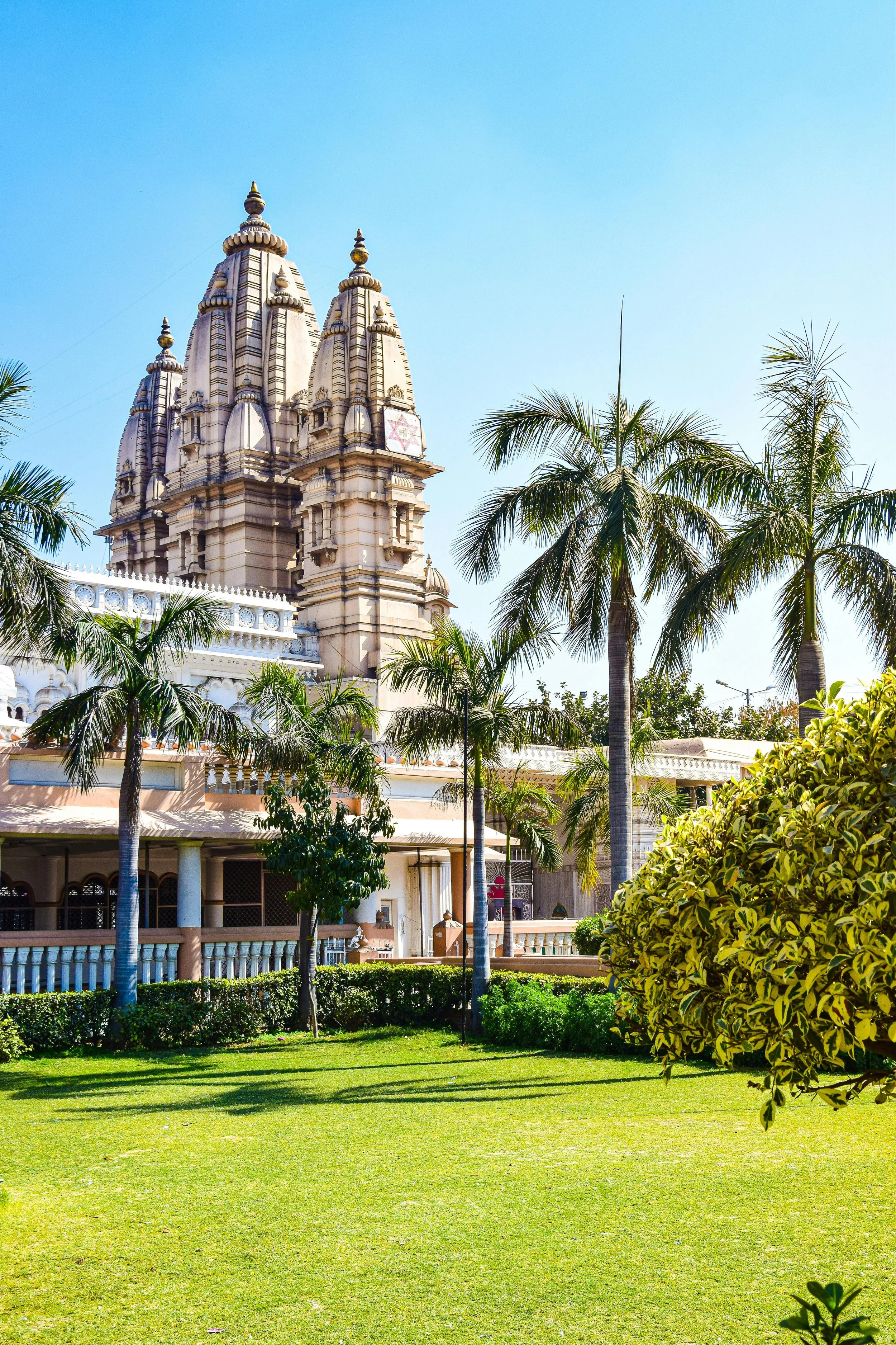 A temple with tall spires, surrounded by palm trees and green grass under a blue sky.