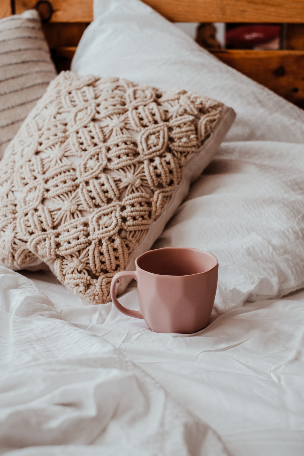 A pink ceramic mug, with decorative pillows and a wooden headboard in the background representing calm and recovery in trauma therapy