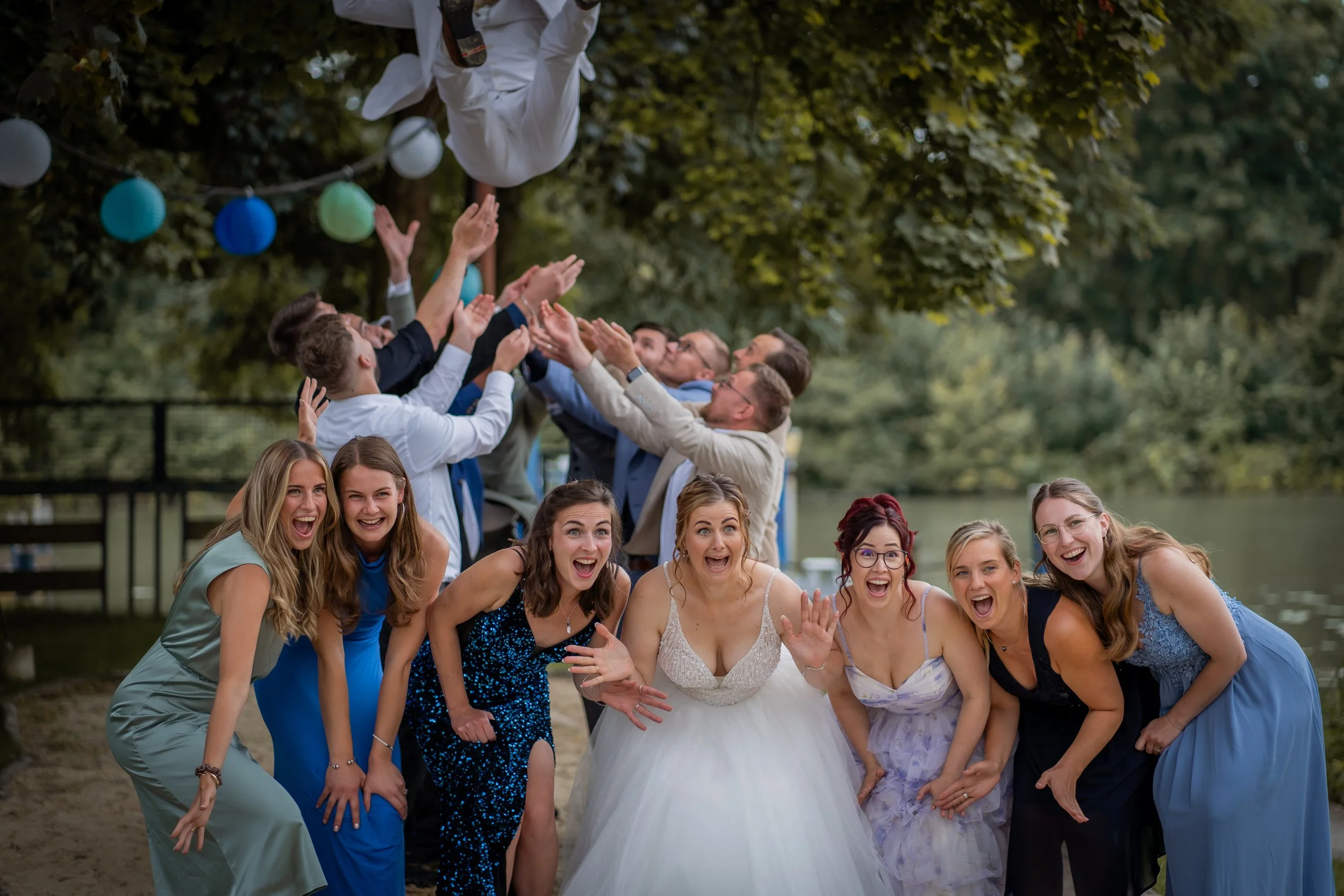 Gruppe lachender Menschen bei einer Hochzeit im Freien, mit Ballons und einem Mann in weißem Anzug, der hoch oben in der Luft schwebt.