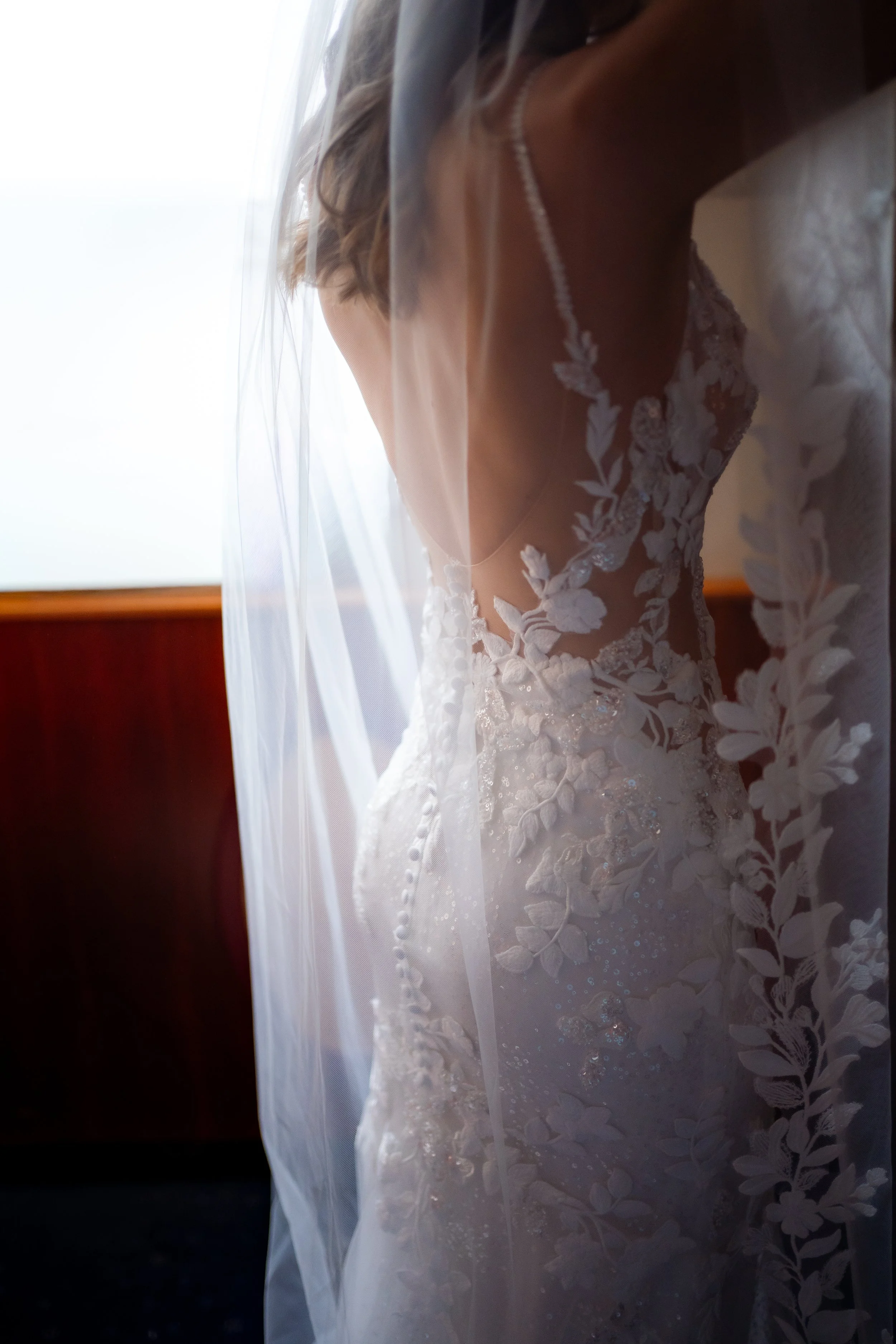 Nahaufnahme eines Hochzeitskleids mit floraler Spitze und Perlen, Blick durch einen Schleier