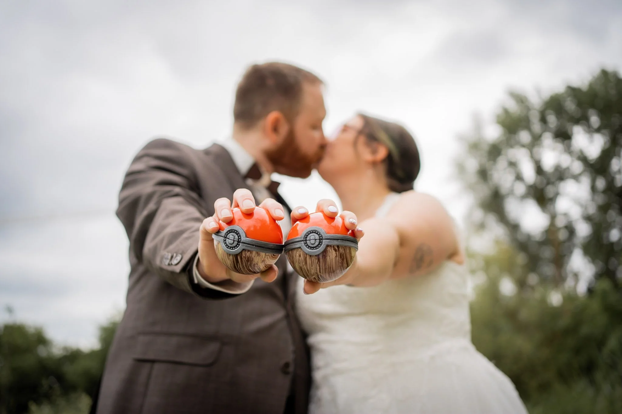 Ein Paar in Hochzeitskleidung küsst sich im Freien, während der Bräutigam Pokémon-Modelle in den Händen hält.