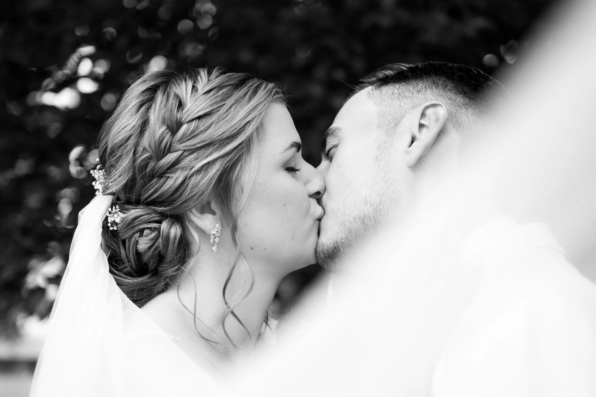 Braut und Bräutigam küssen sich bei ihrer Hochzeit im Freien, in Schwarz-Weiß-Fotografie.