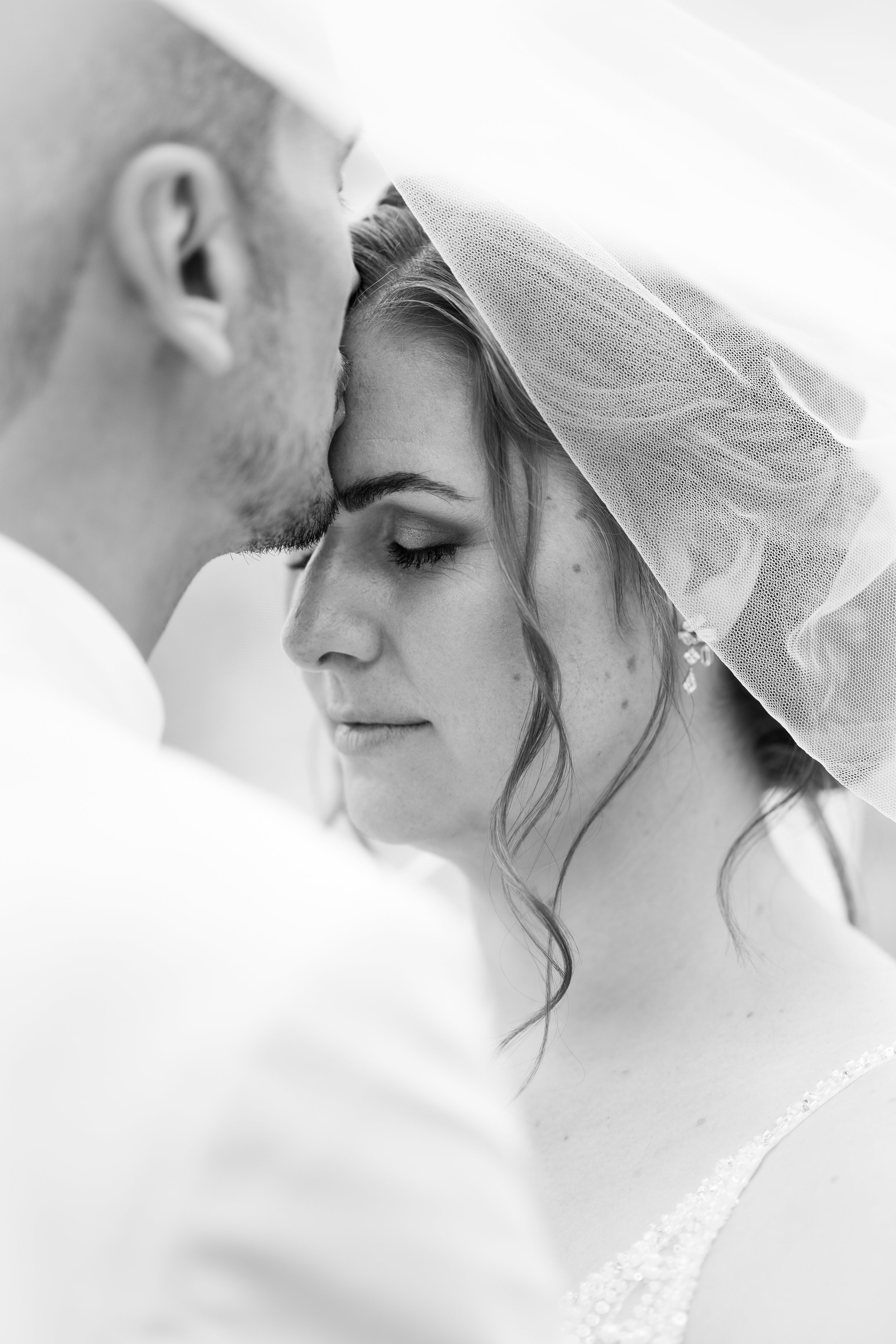 Schwarz-weiße Nahaufnahme eines Mannes und einer Frau, die sich bei ihrer Hochzeit küssen, mit dem Blick auf die Frau, die einen breiten Schleier trägt.