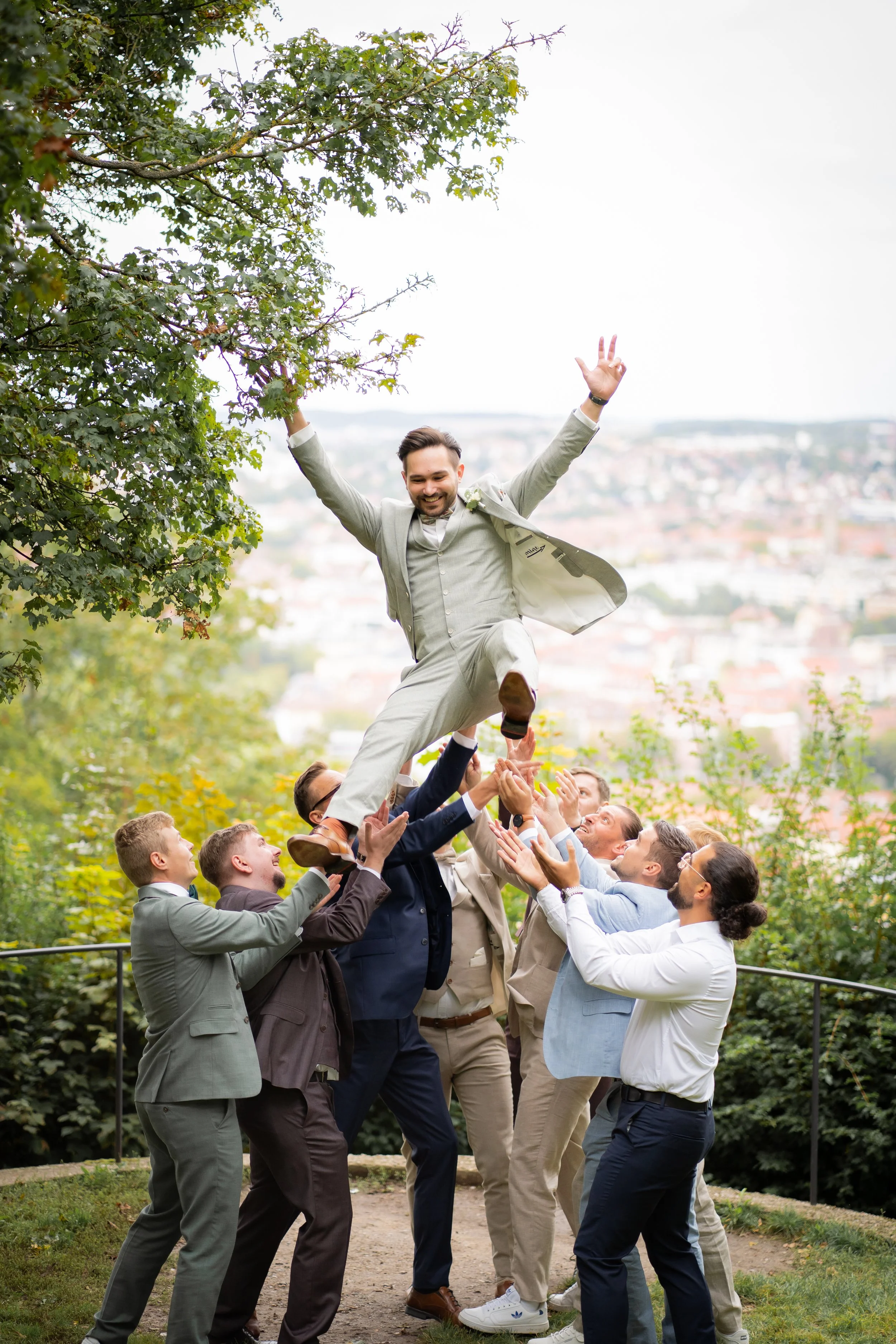 Männer unterstützen Männer beim Aufbau eines menschlichen Turms im Park, während die Gruppe lacht und Spaß hat.
