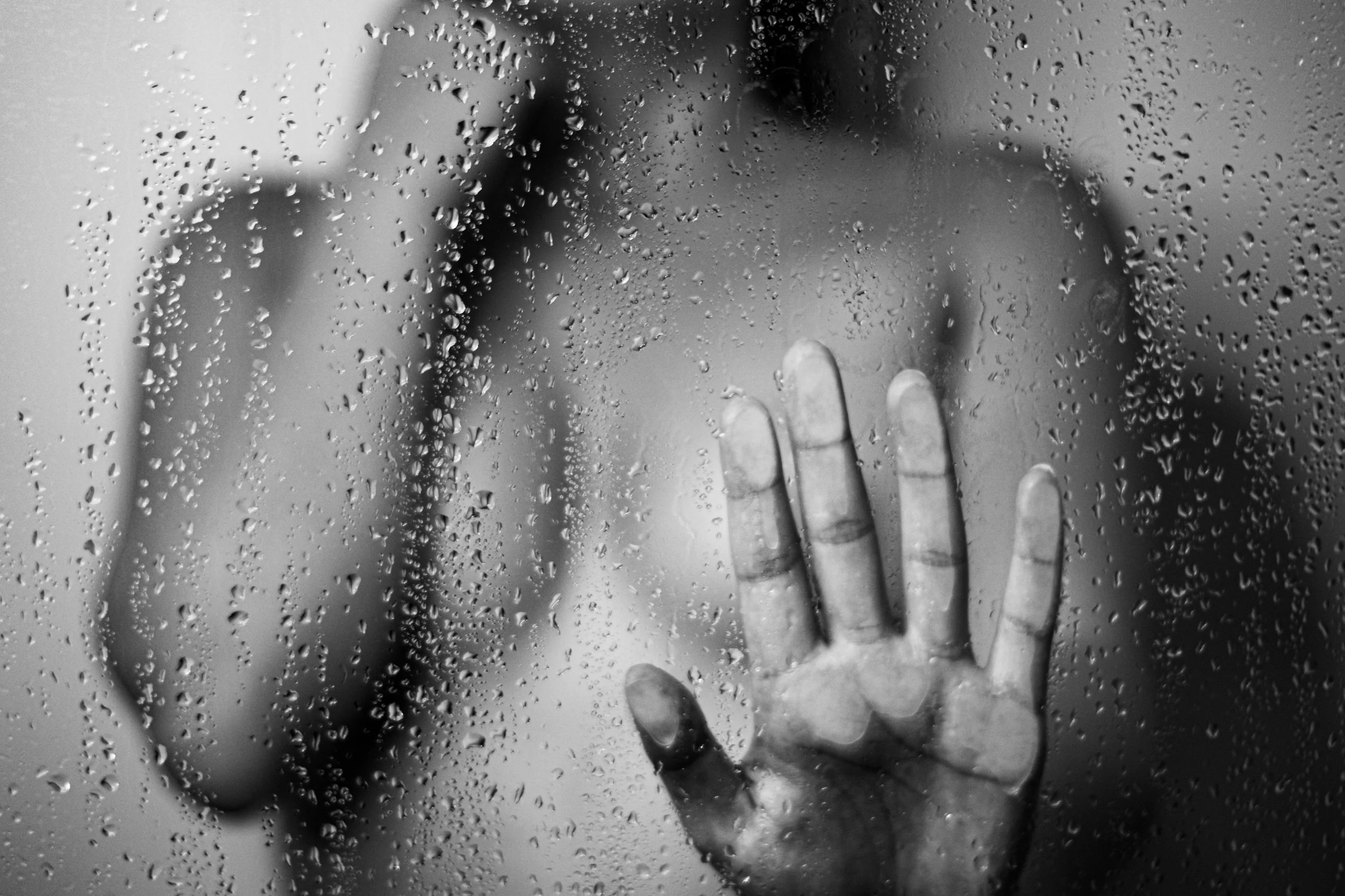 Hand berührt eine glasscheibe mit Regentropfen darauf, Menschen sind im Hintergrund sichtbar, unscharf. Boudoir, Akt, Sinnliche Fotoshooting, Senusalshooting