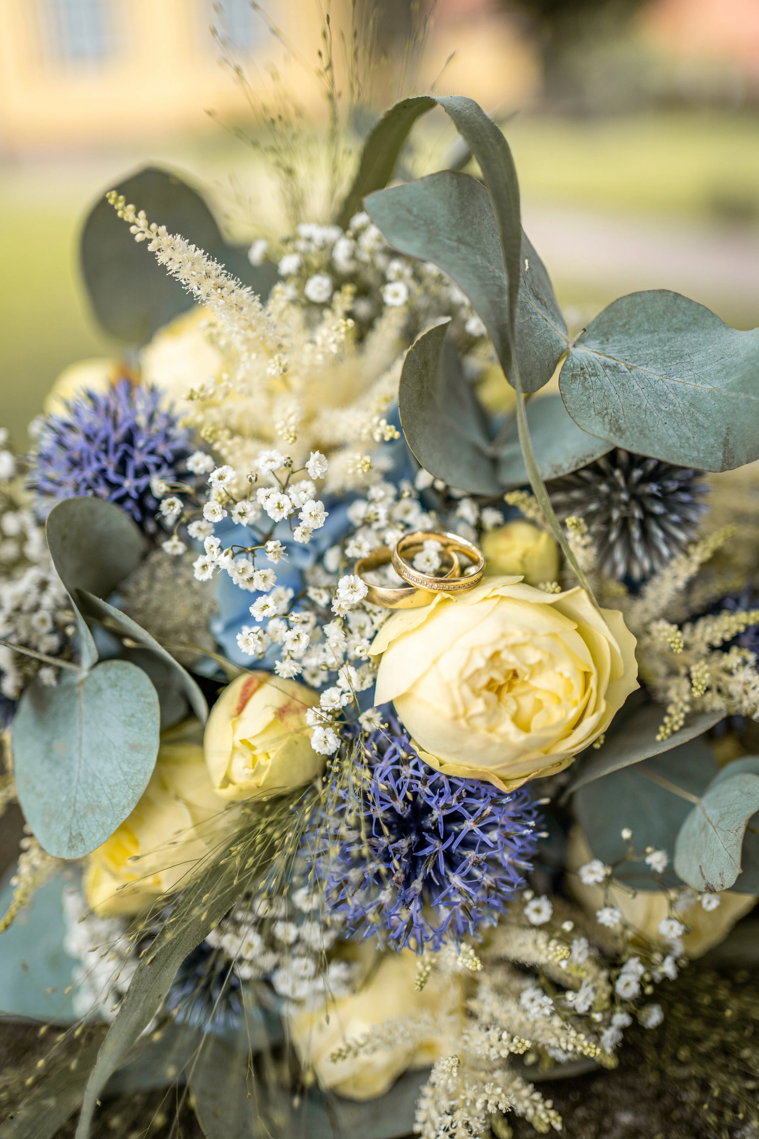 Eine Blumenstrauß mit weißen, lila und gelben Blumen, inklusive Eukalyptusblättern und goldenen Ringen.