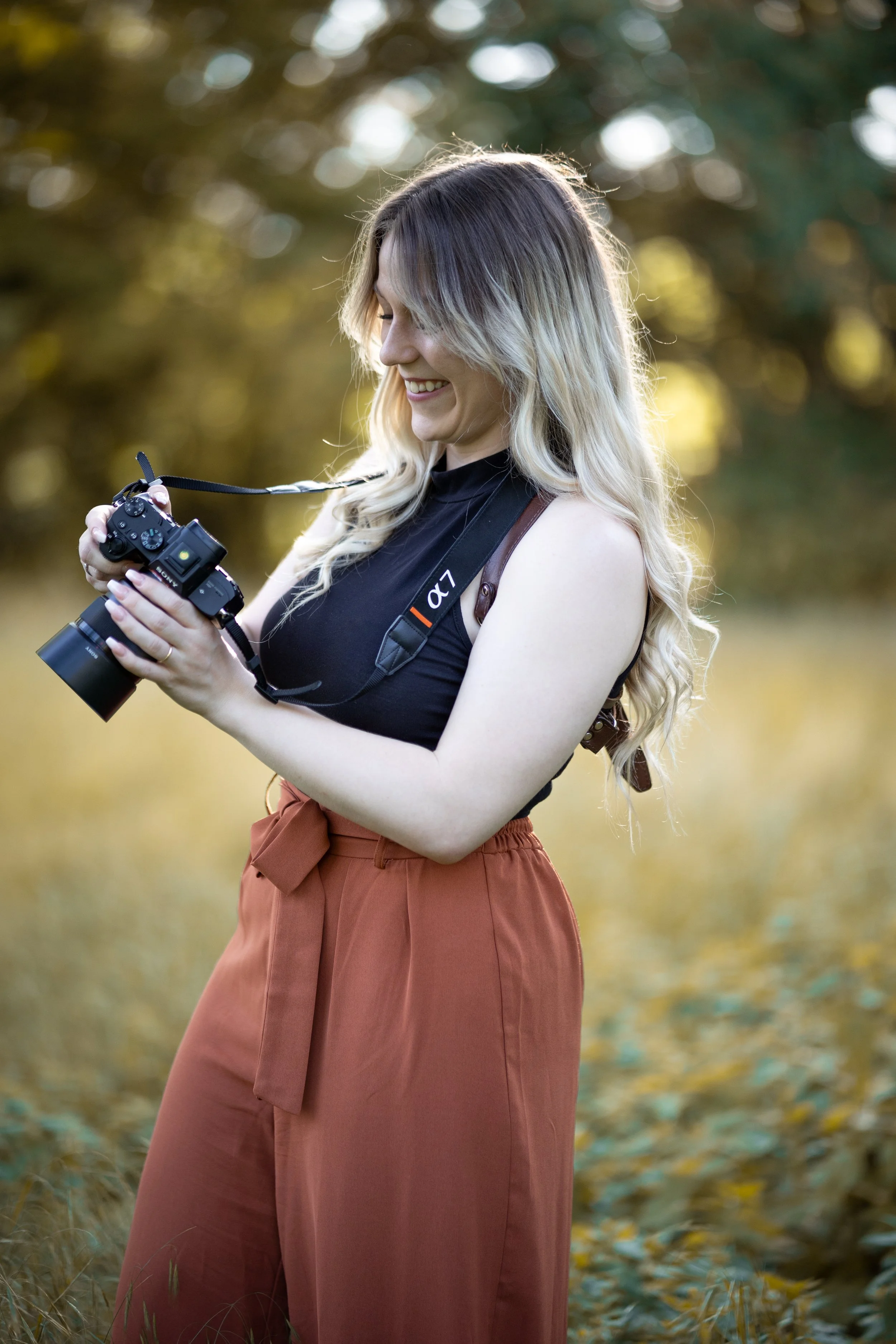 Die Fotografin mit braunen, weinroten Hosen und schwarzen Top, die in einer Herbstlandschaft mit goldenen Blättern ein Fotoshooting fotografiert, sie hat zwei Sony Kameras um.