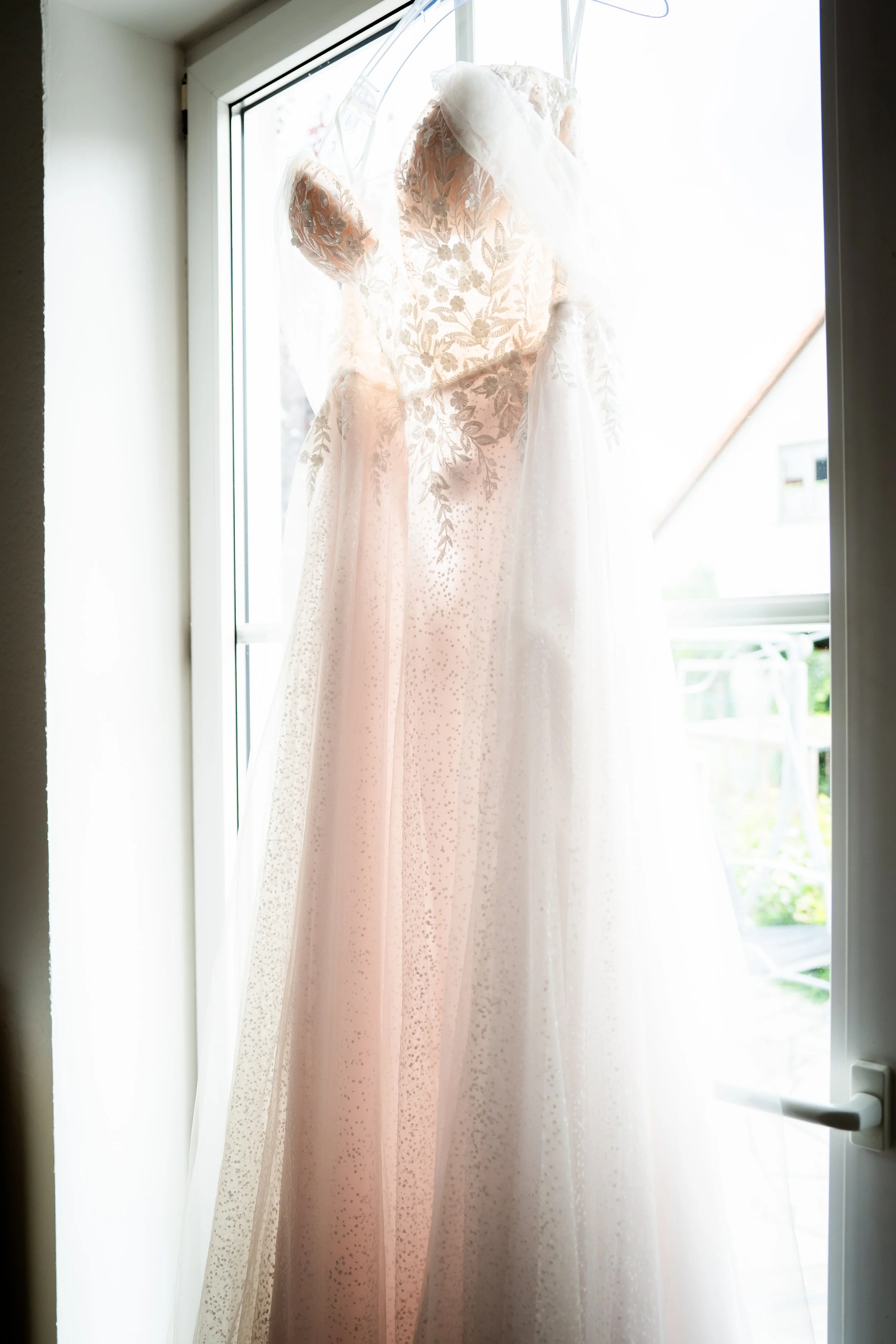 Hintergrund mit einem weißen Brautkleid, das vor einem Fenster hängt.
