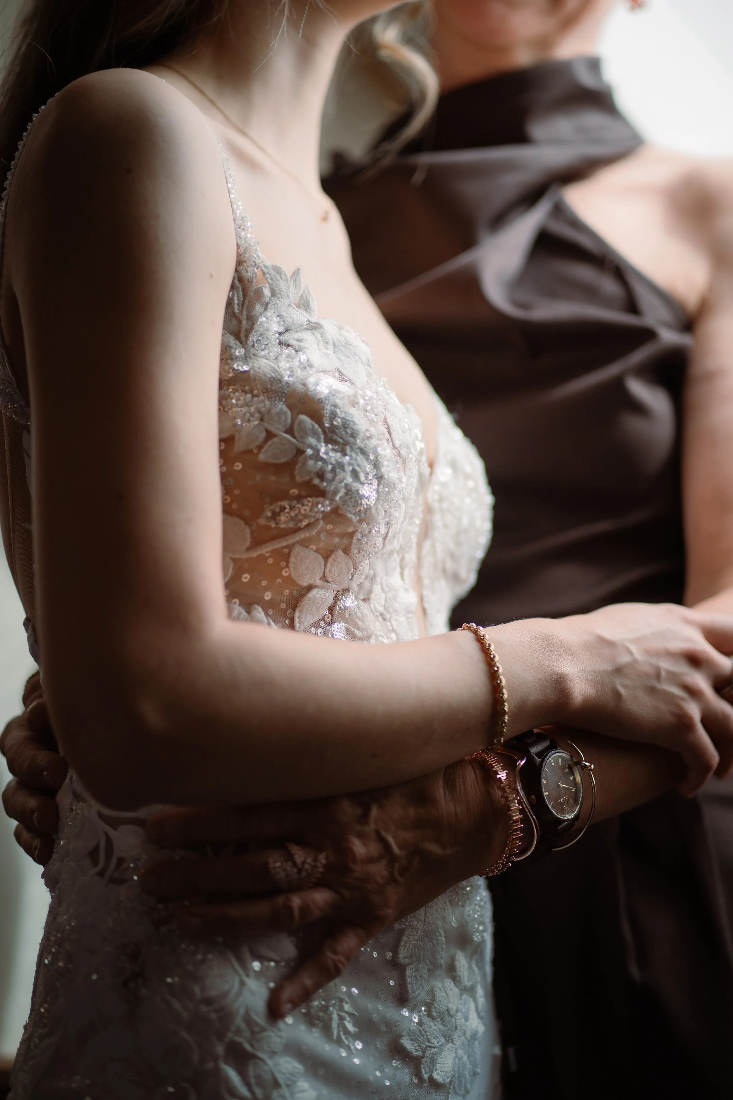 Nahaufnahme von zwei Frauen bei einer Umarmung, eine trägt ein weißes Spitzenkleid, vermutlich Braut, die andere trägt ein dunkles Kleid, vermutlich Brautmutter oder Begleitperson.