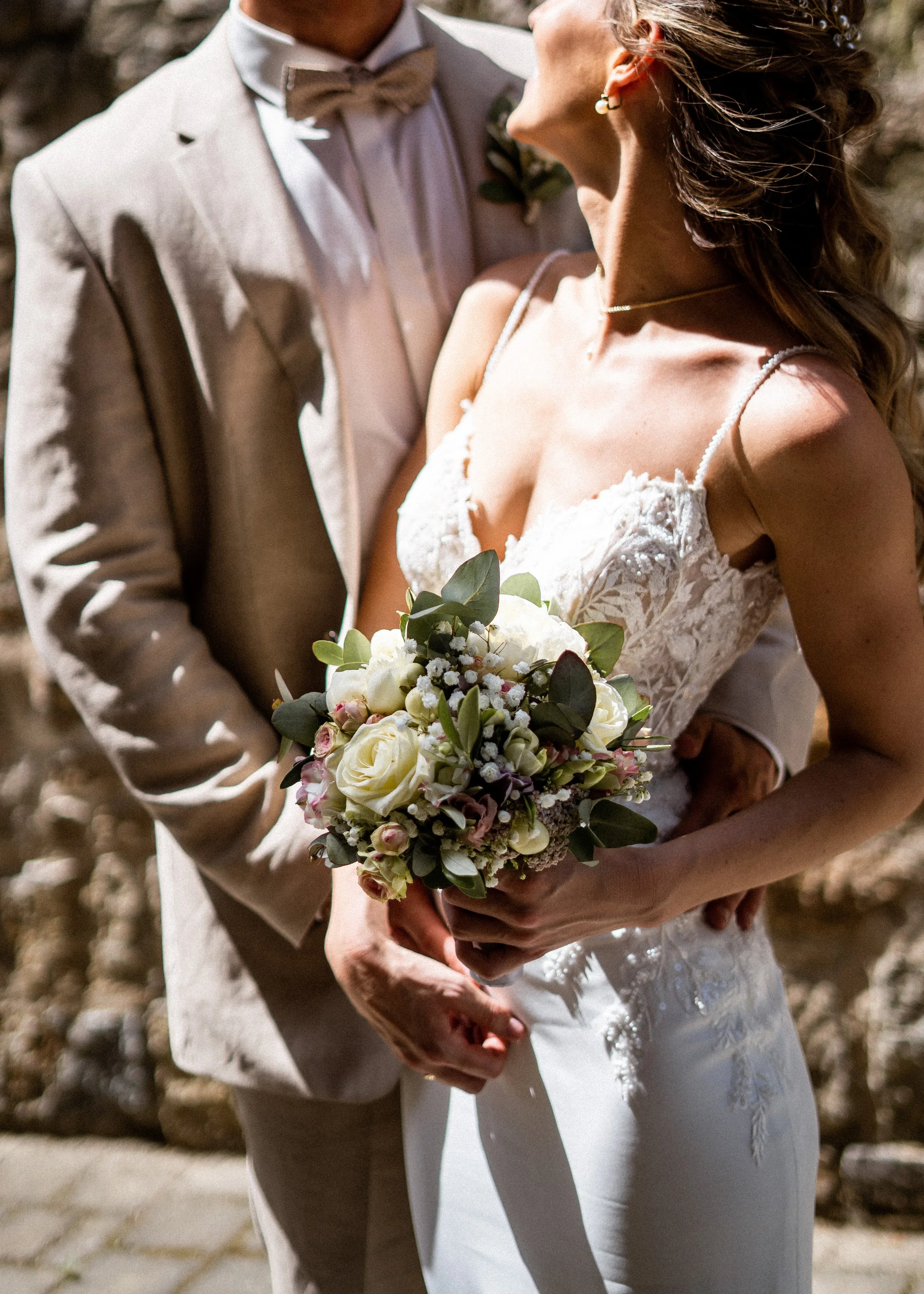 Ein Brautpaar bei einer Hochzeit, die Braut hält einen Blumenstrauß und trägt ein weißes Hochzeitskleid, der Bräutigam trägt einen hellen Anzug mit Fliege.