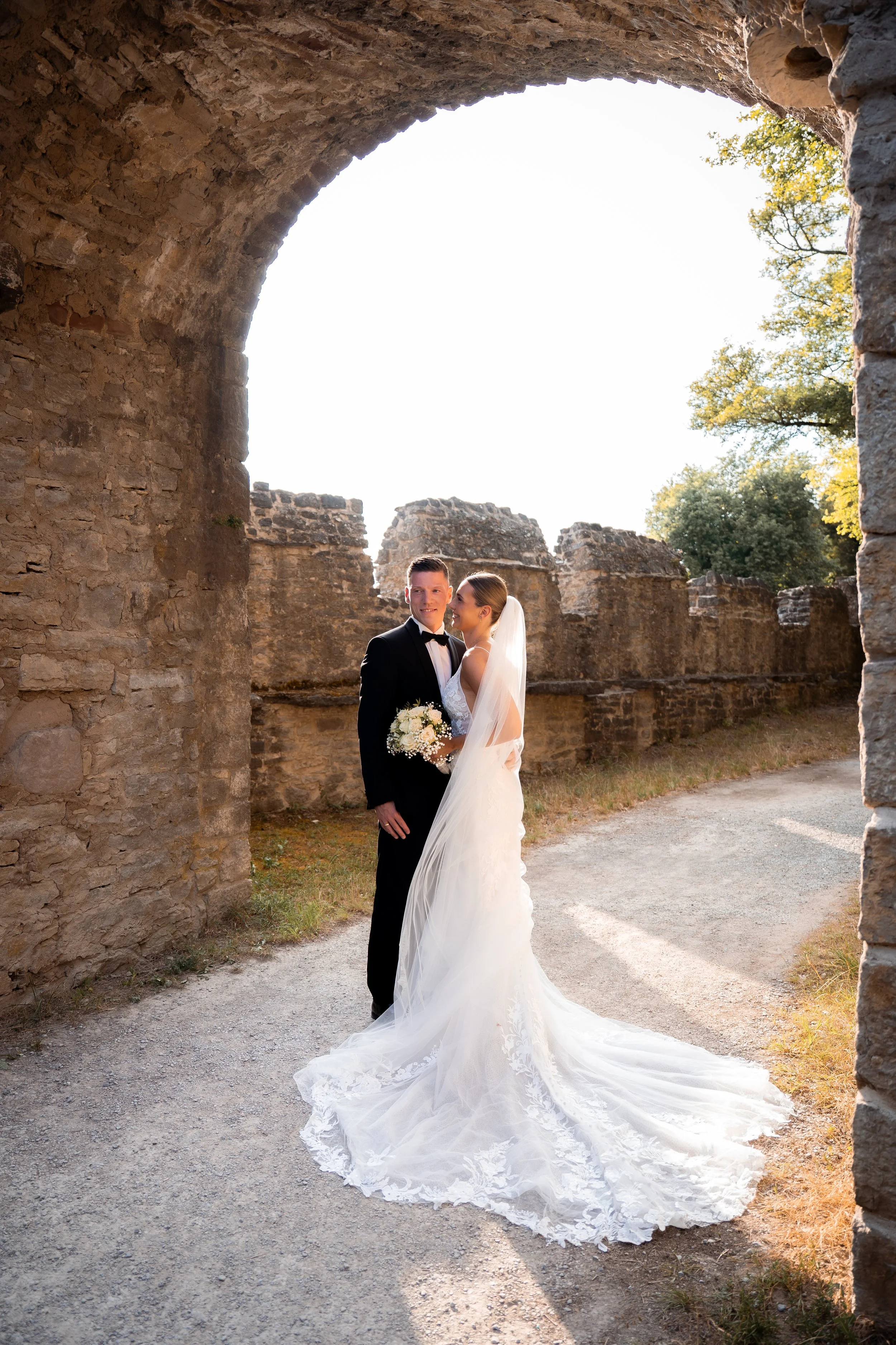Braut und Bräutigam in Hochzeitskleid und Anzug vor alten Ruinen bei Sonnenuntergang.