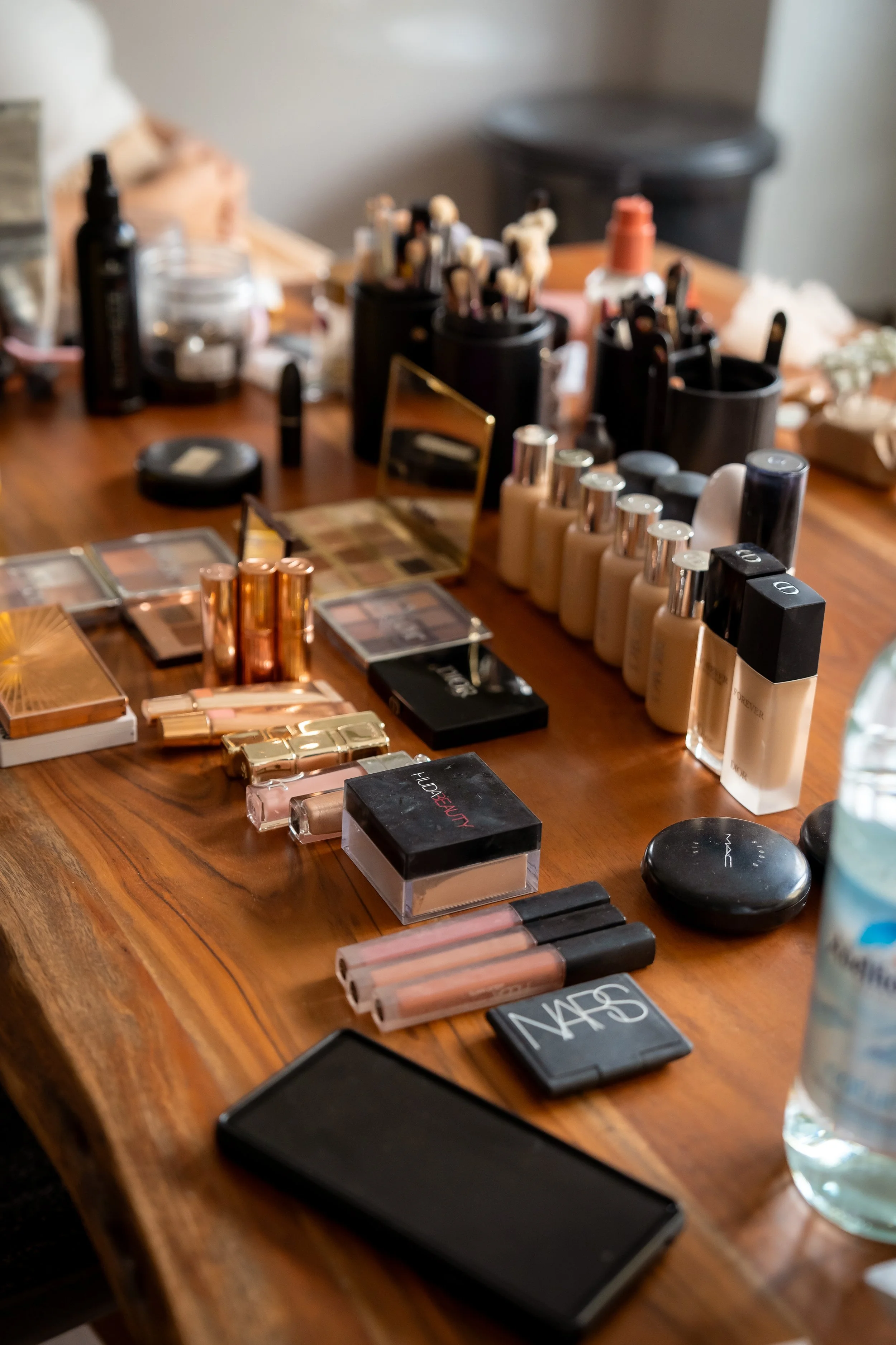 Ein Holztisch mit verschiedenen Make-up-Produkten, Kosmetiktiegeln, Lippenstiften, Make-up-Paletten, Foundation-Flaschen, Puder-Kompressen, Kosmetiktüchern und Make-up-Werkzeugen.