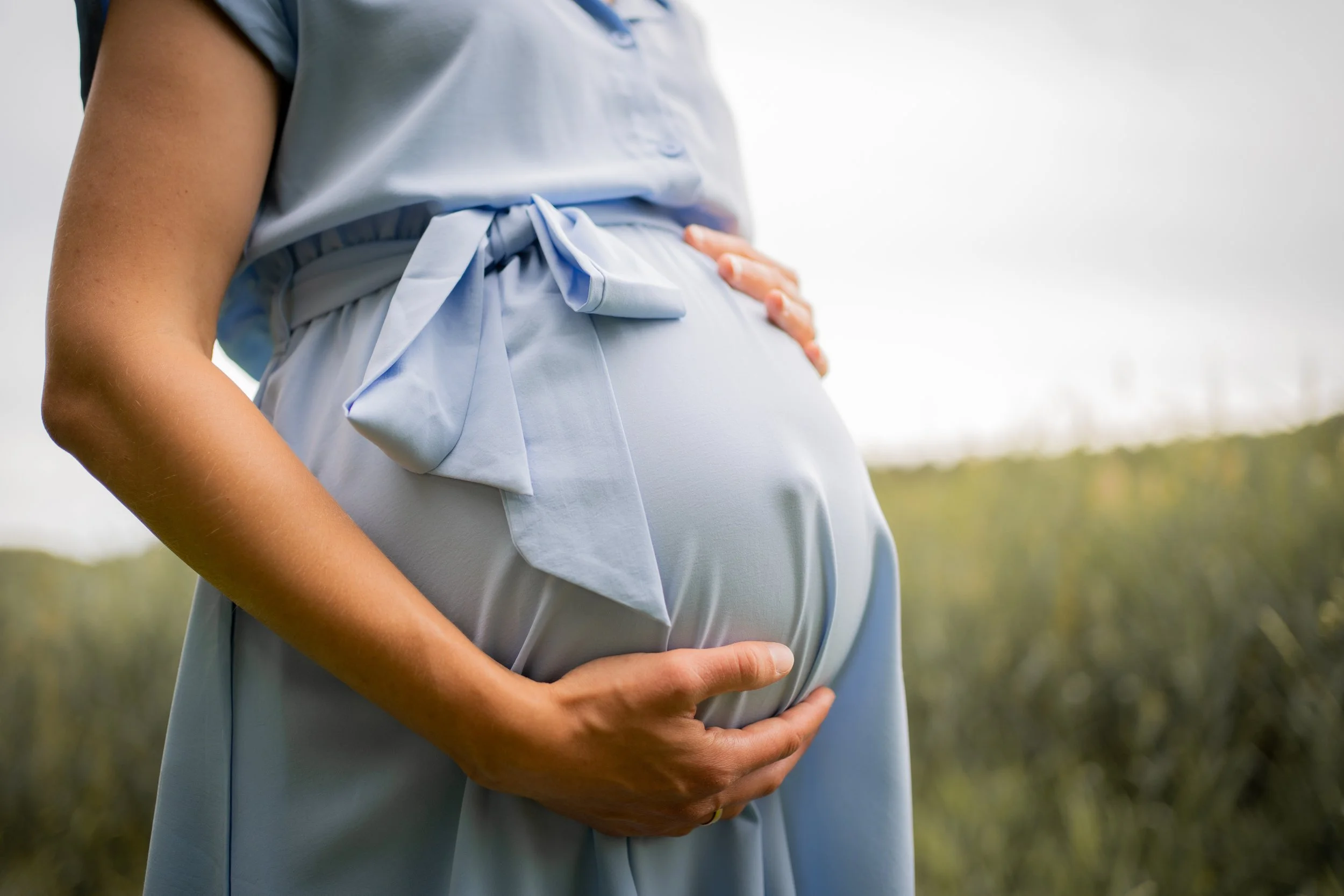 Schwangere Frau hält ihre Hand auf den Babybauch im Freien.
