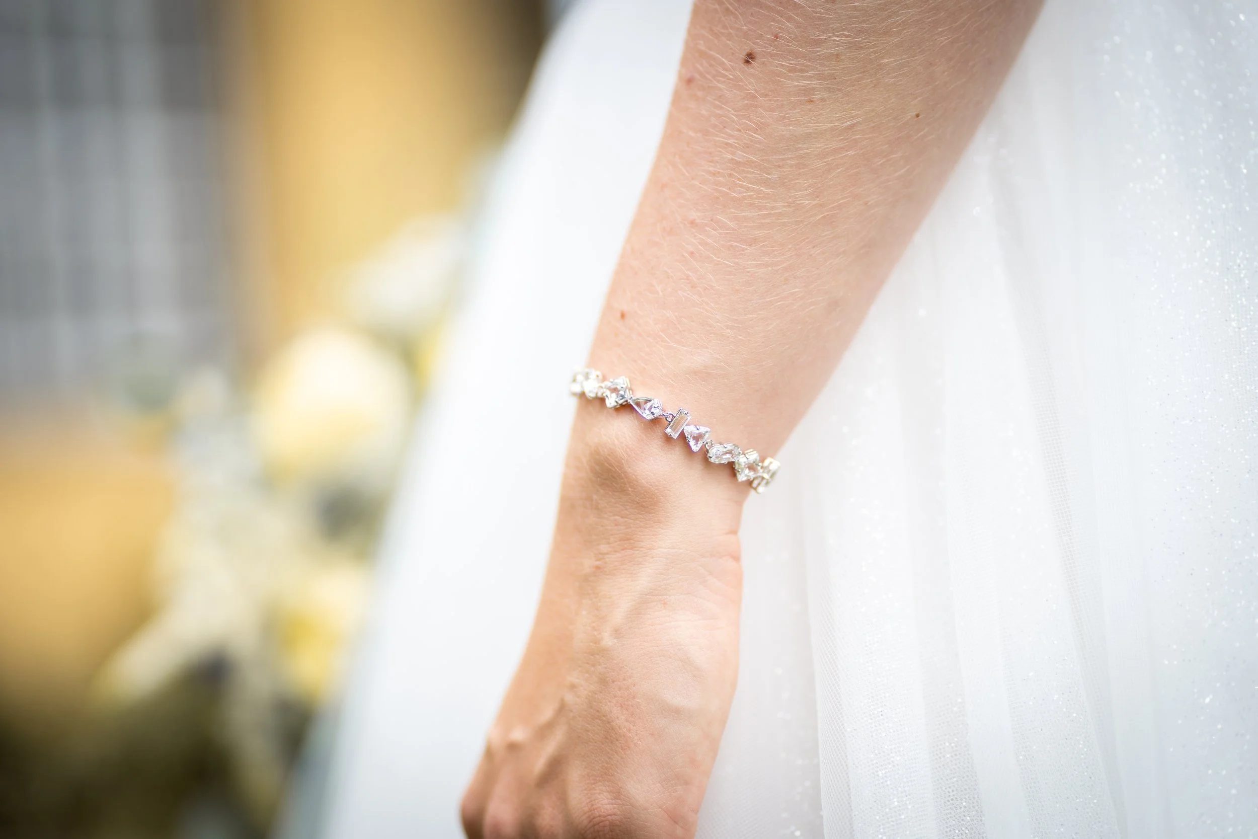 Nahaufnahme eines Arms mit einem silbernen Armband, vor einem weißen Hintergrund, möglicherweise bei einer Feier oder Hochzeit.