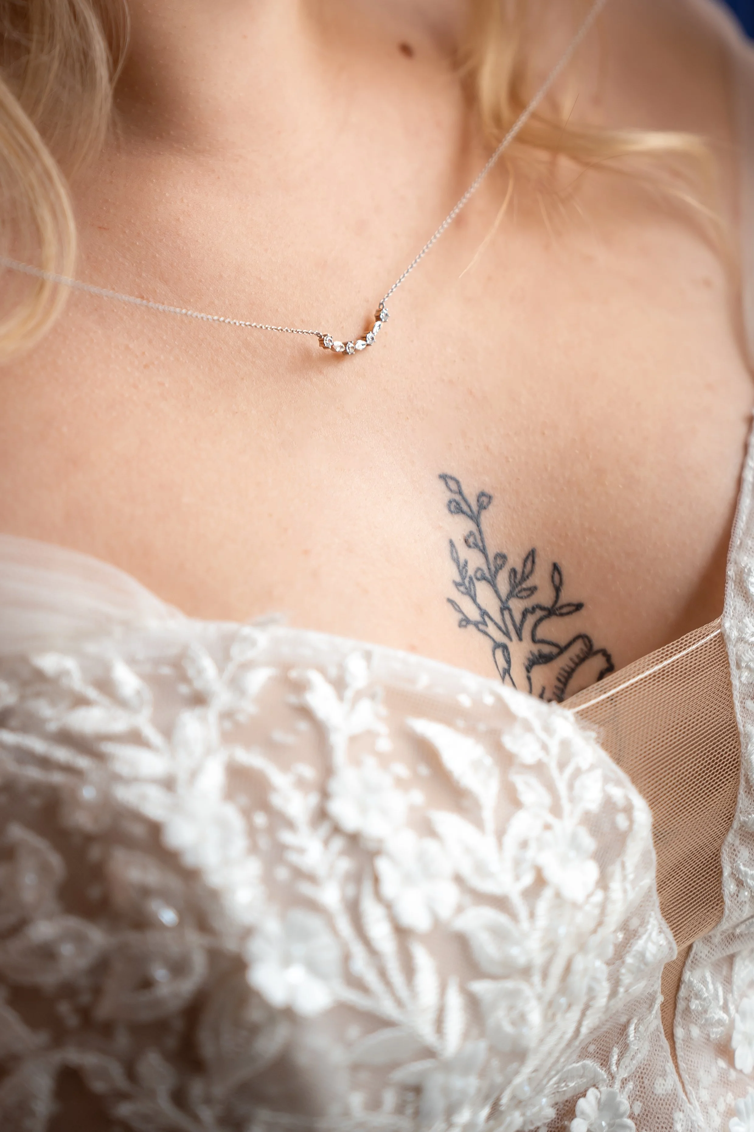 Nahaufnahme eines Körpers mit einer silbernen Halskette mit zehn Edelsteinen und einer Tattoo-Blume auf der Haut.
