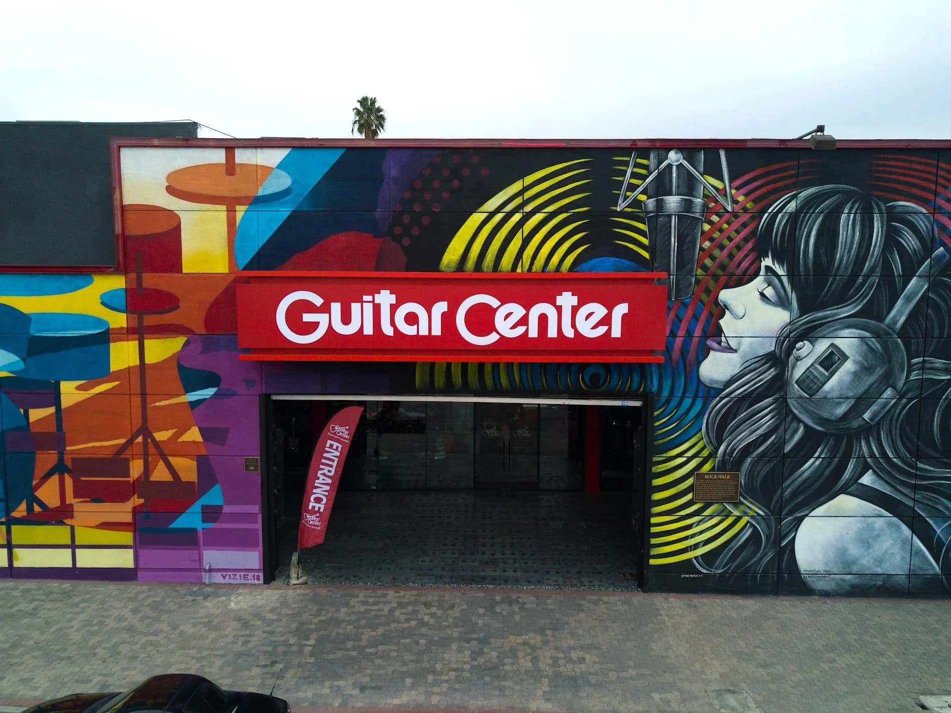 Commercial retail storefront mural at Guitar Center in Los Angeles featuring a singer, studio microphone, and bold abstract music graphics across the building facade.