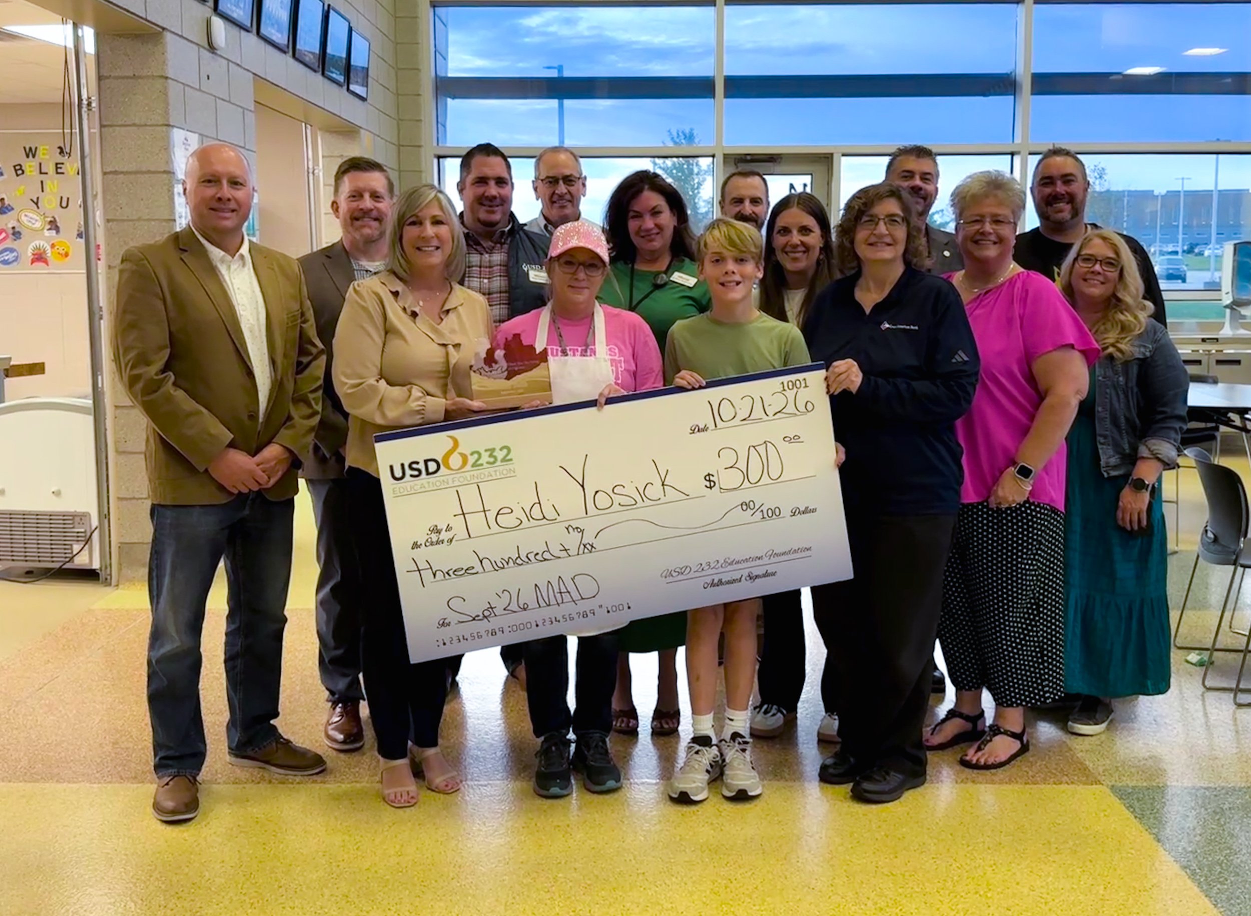 a group of people in a cafeteria holding a large check for $300