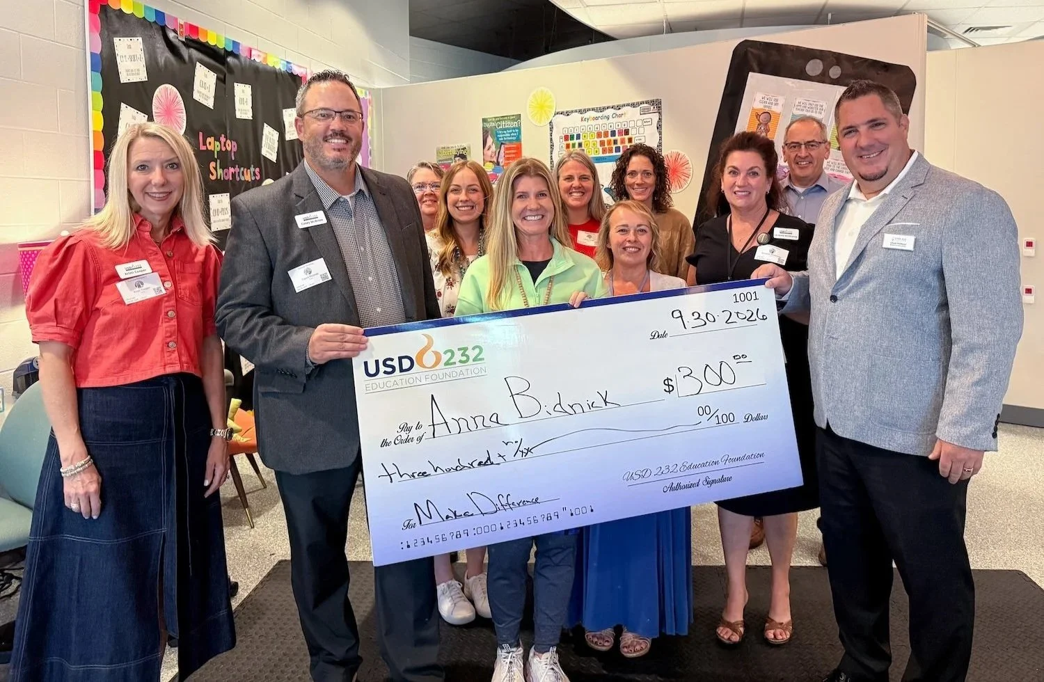 a group of people in a classroom holding a large check for $300