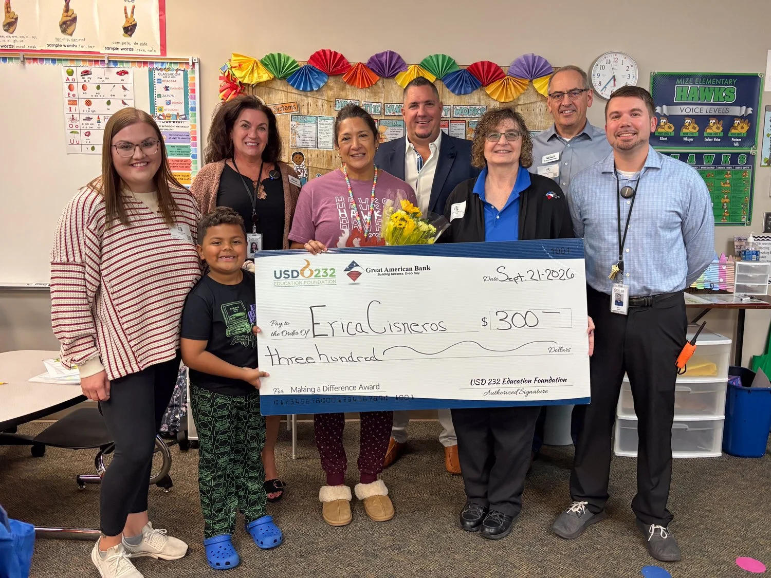 a group of adults and a child stand behind a large check in a classroom
