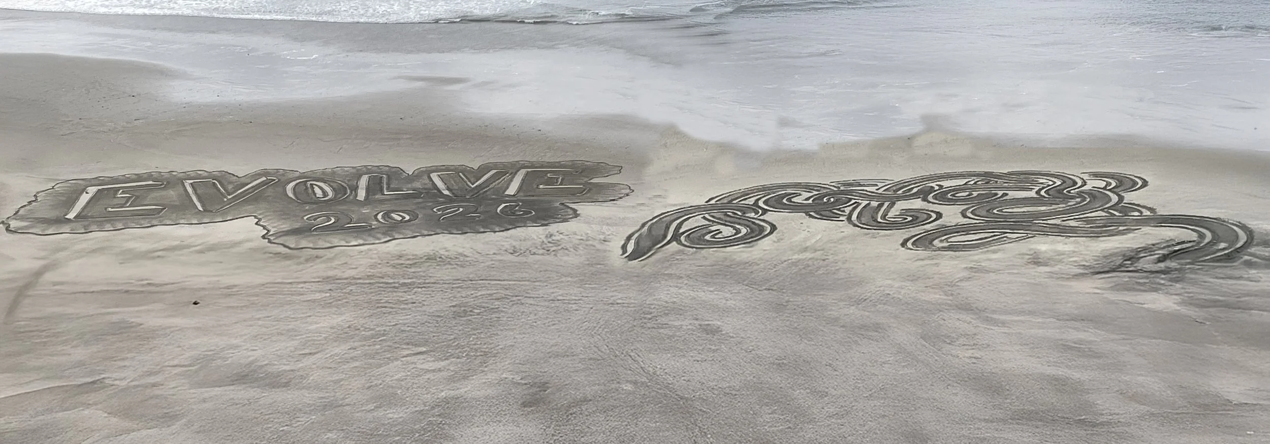 Sand art on the beach with the words 'Evolve 2026' and decorative swirls.