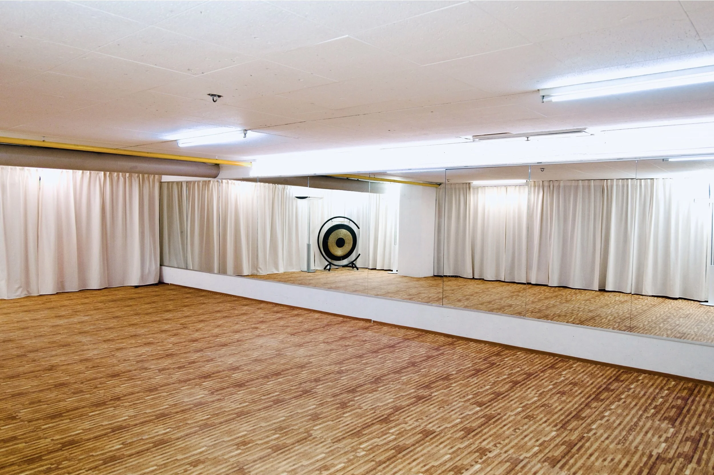 Ein leeres Tanzstudio mit Spiegeln an der Wand, Holzboden und einer Chime in der Ecke.