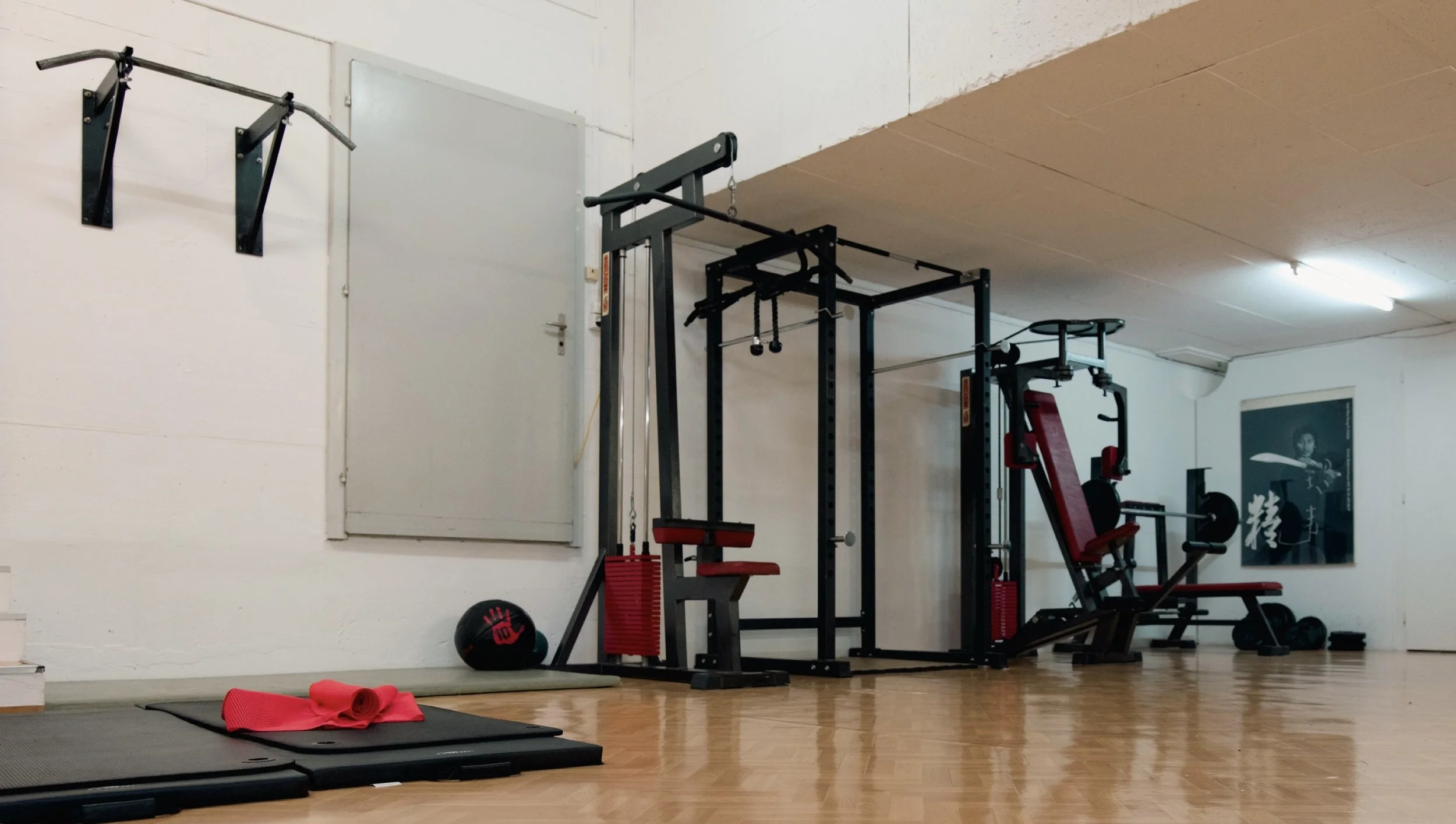Krafttrainingsgeräte in einem Fitnessraum, darunter eine Sitzbank, Hanteln, Jumping-Kasten, Medizinball und Yoga-Matte.