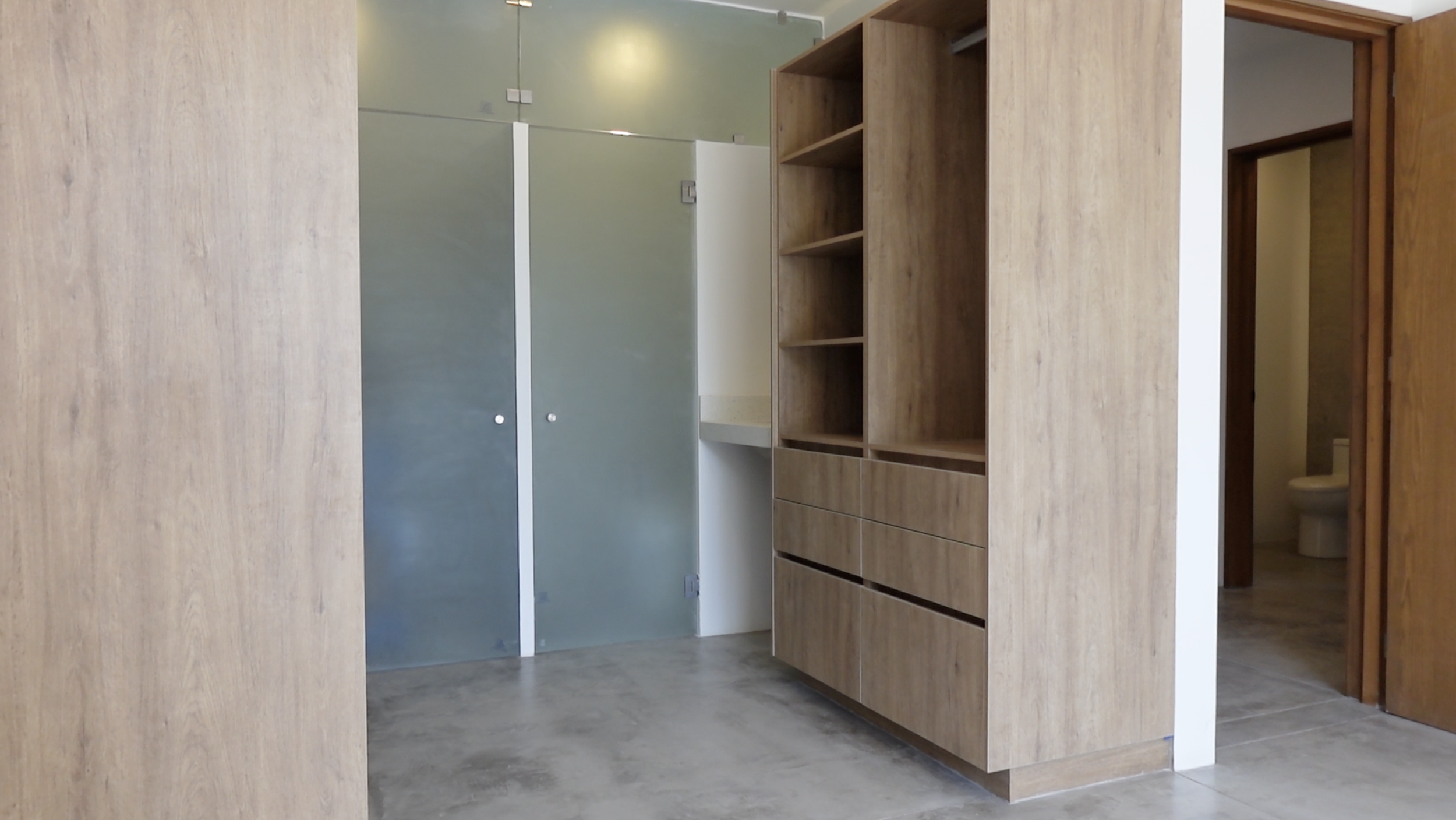Vista de un espacio interior con paredes y mobiliario de madera, incluyendo estanterías y puertas, y un acceso a un baño visible al fondo.