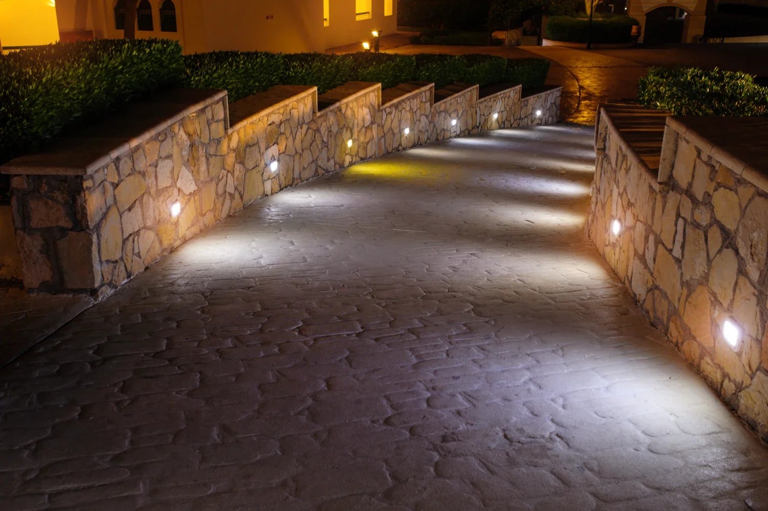 Curved natural stone retaining wall in Seattle, WA with integrated low-voltage hardscape lighting along a stone paver walkway at night.