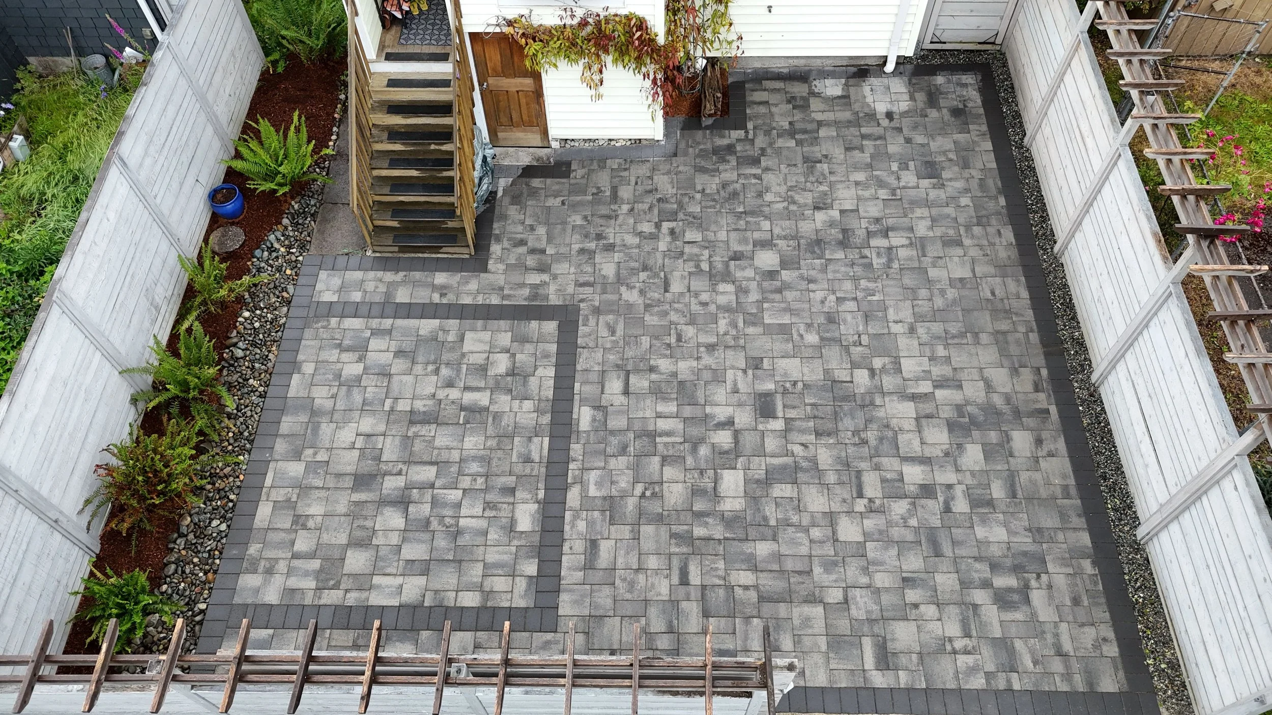 Multi-tone gray paver patio installation in Kirkland, WA with a dark border accent leading to wooden deck steps and a back entry.