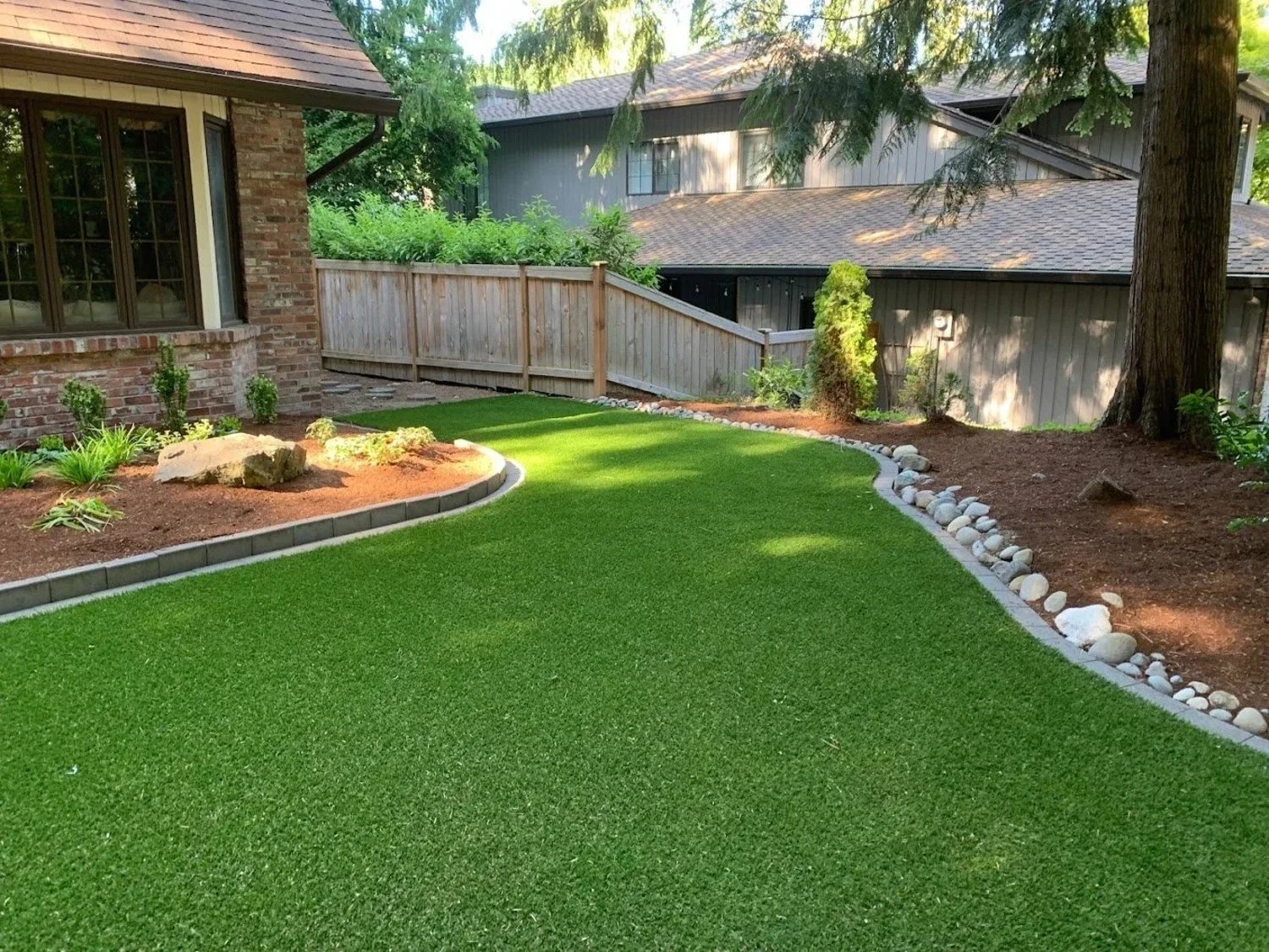 Backyard artificial turf installation in Seattle, WA with stone-bordered beds and wood fencing