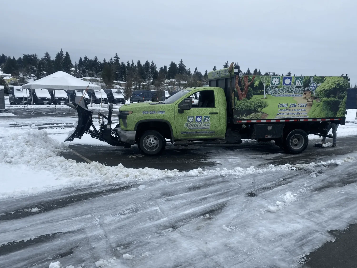 North East Landscaping green plow truck clearing snow from a commercial parking lot in Kent, WA.