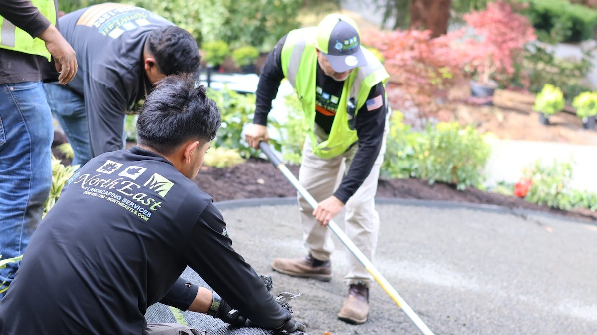 North East Landscaping Services crew preparing the base and laying artificial turf beside fresh planting beds in Renton, WA