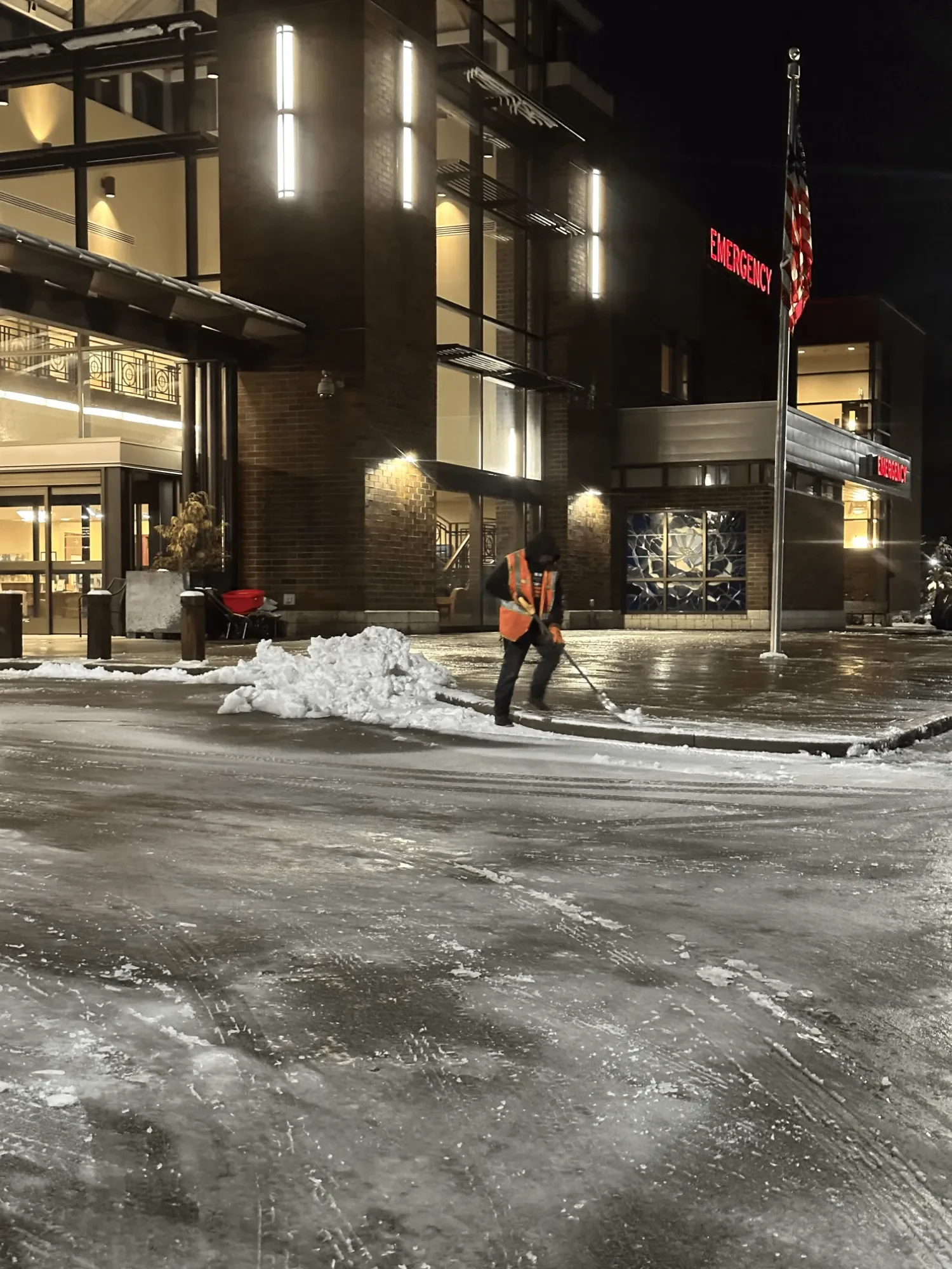 North East Landscaping crew clearing the sidewalk at a hospital emergency entrance in Kent, WA, at night.